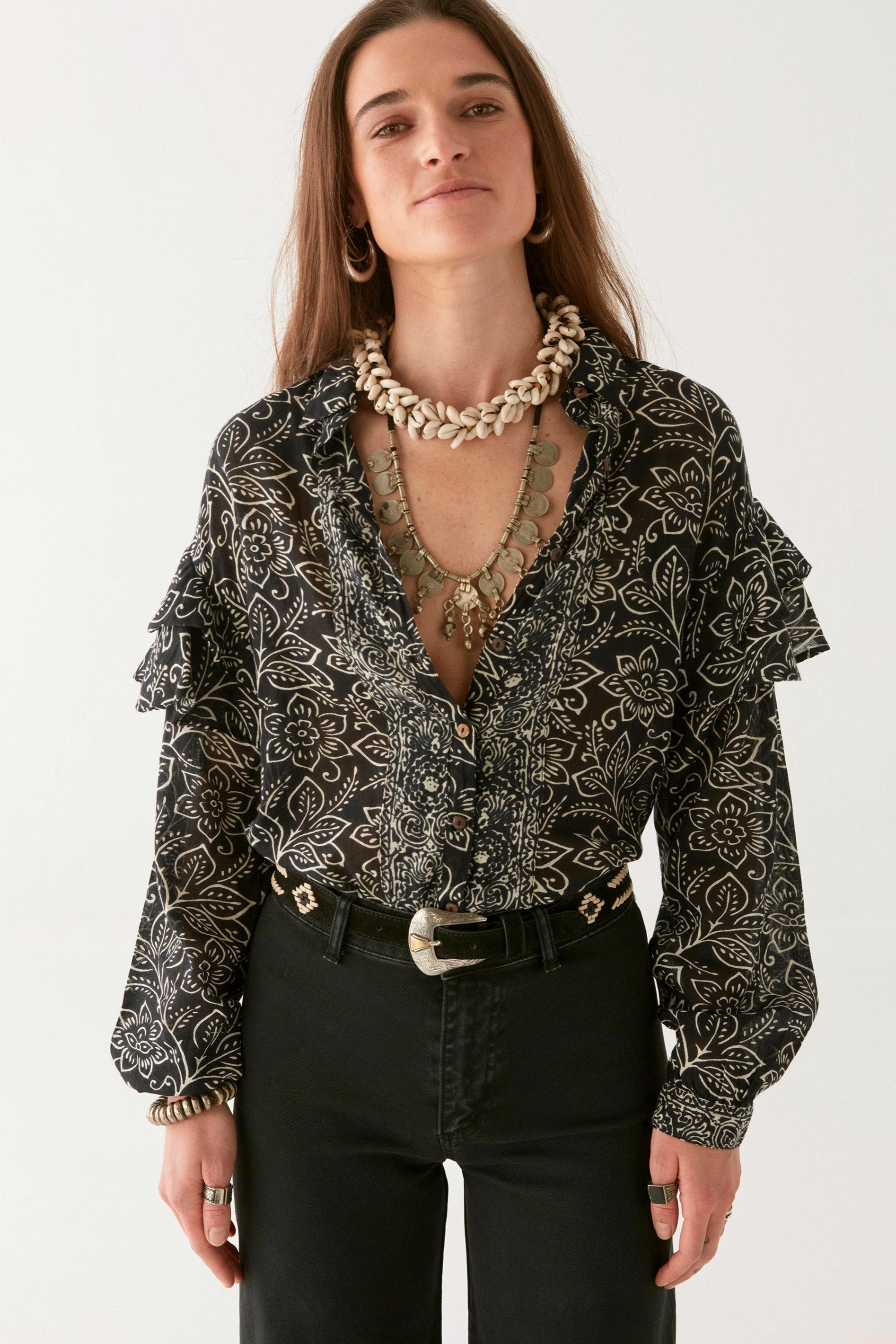 Woman wearing a black and ivory floral patterned blouse, black pants, and boots on a white background. 