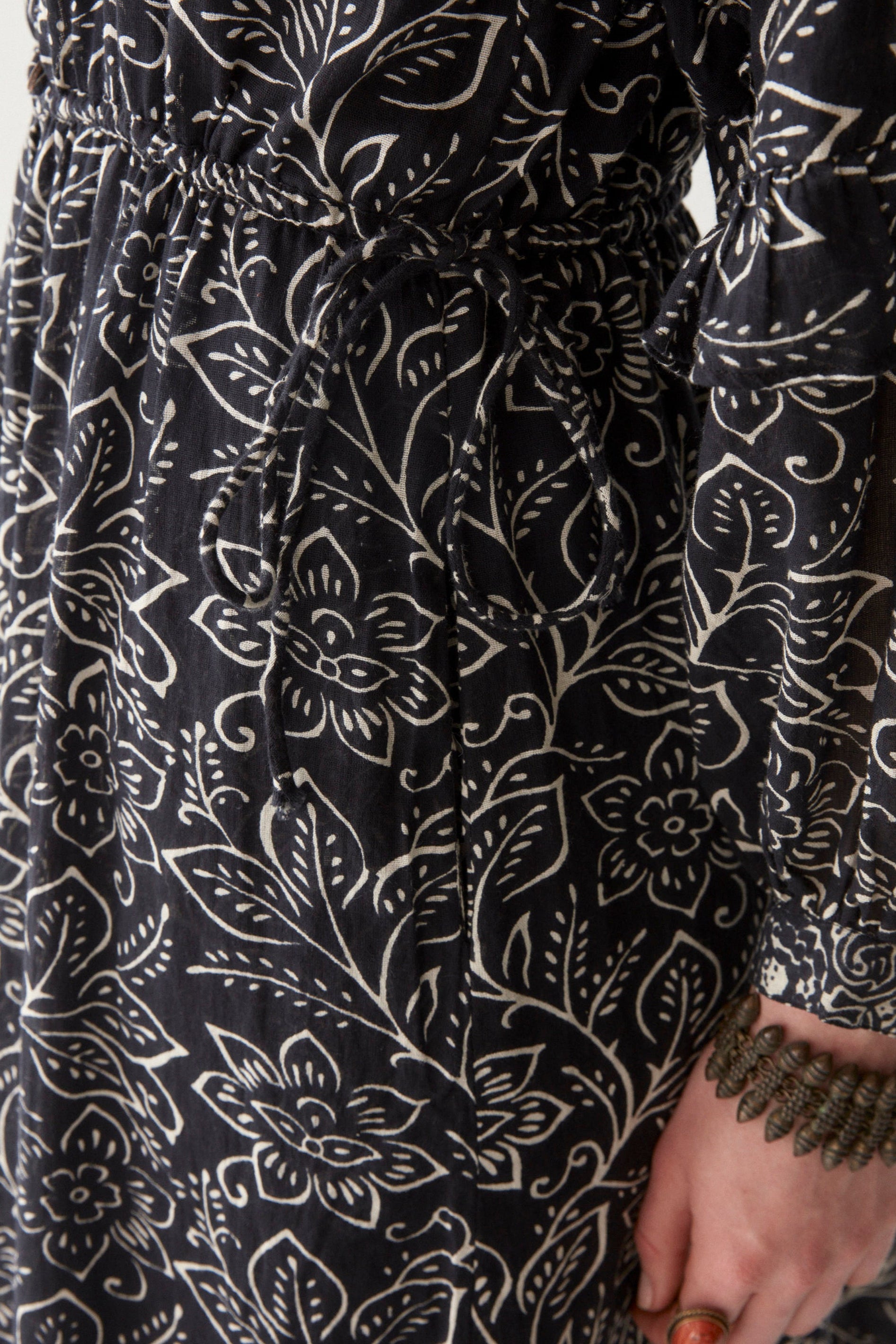 Woman wearing a black and white floral patterned maxi dress against a white background. up close to show tie detail at waist.  