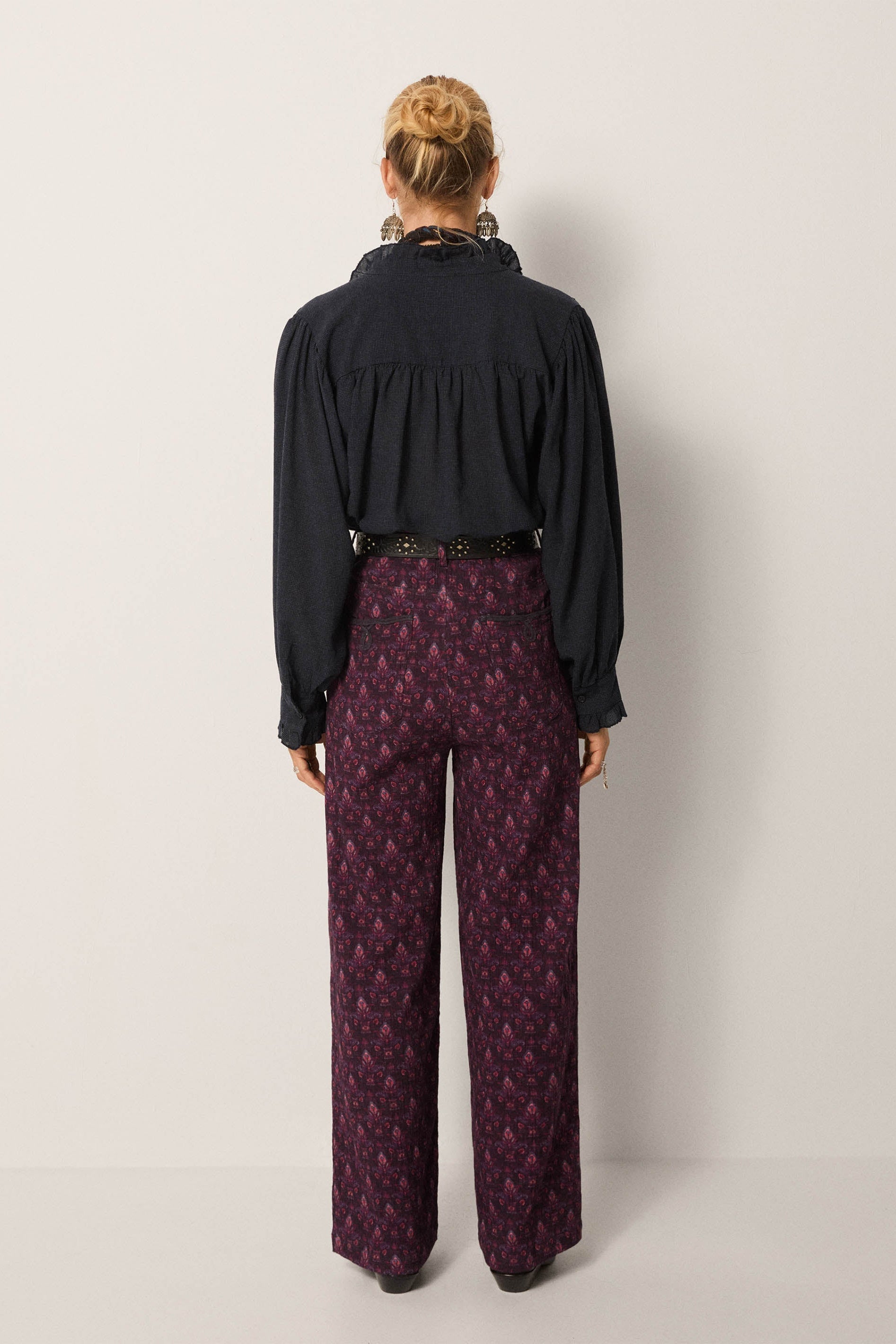Person wearing a black blouse and patterned purple pants against a white background