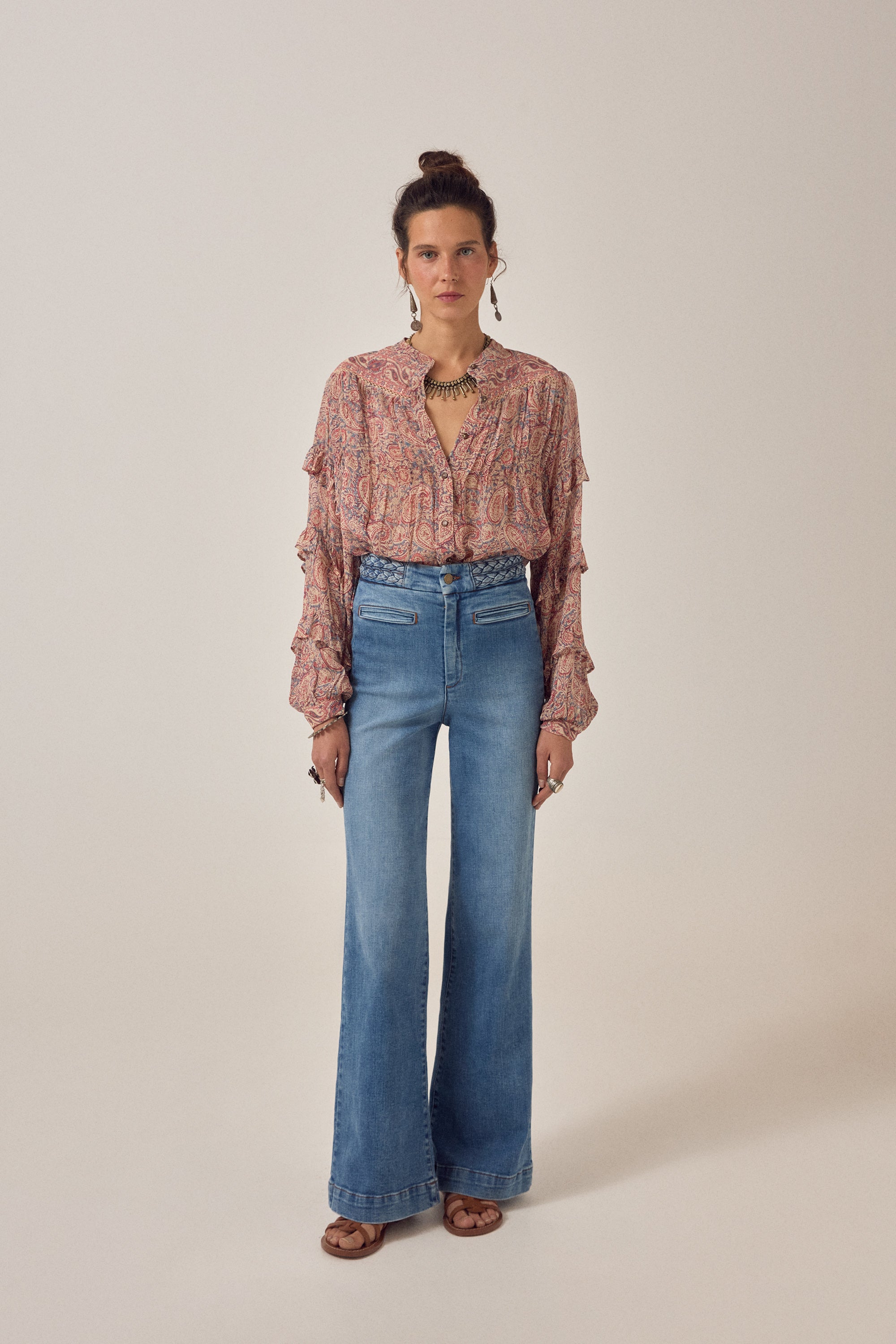 Women wearing a  floral patterned blouse and blue jeans on a plain background