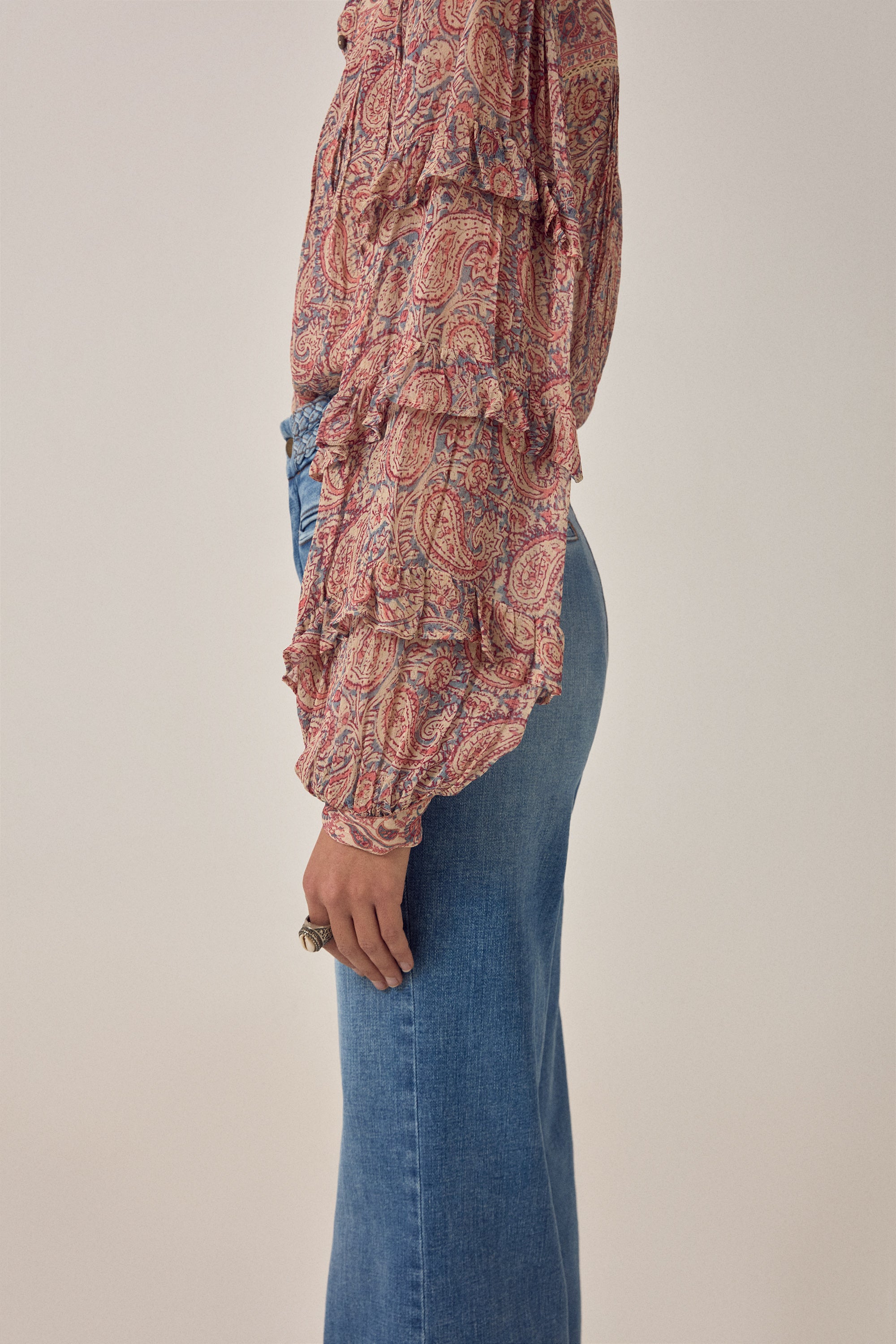 Women wearing a  floral patterned blouse and blue jeans on a plain background