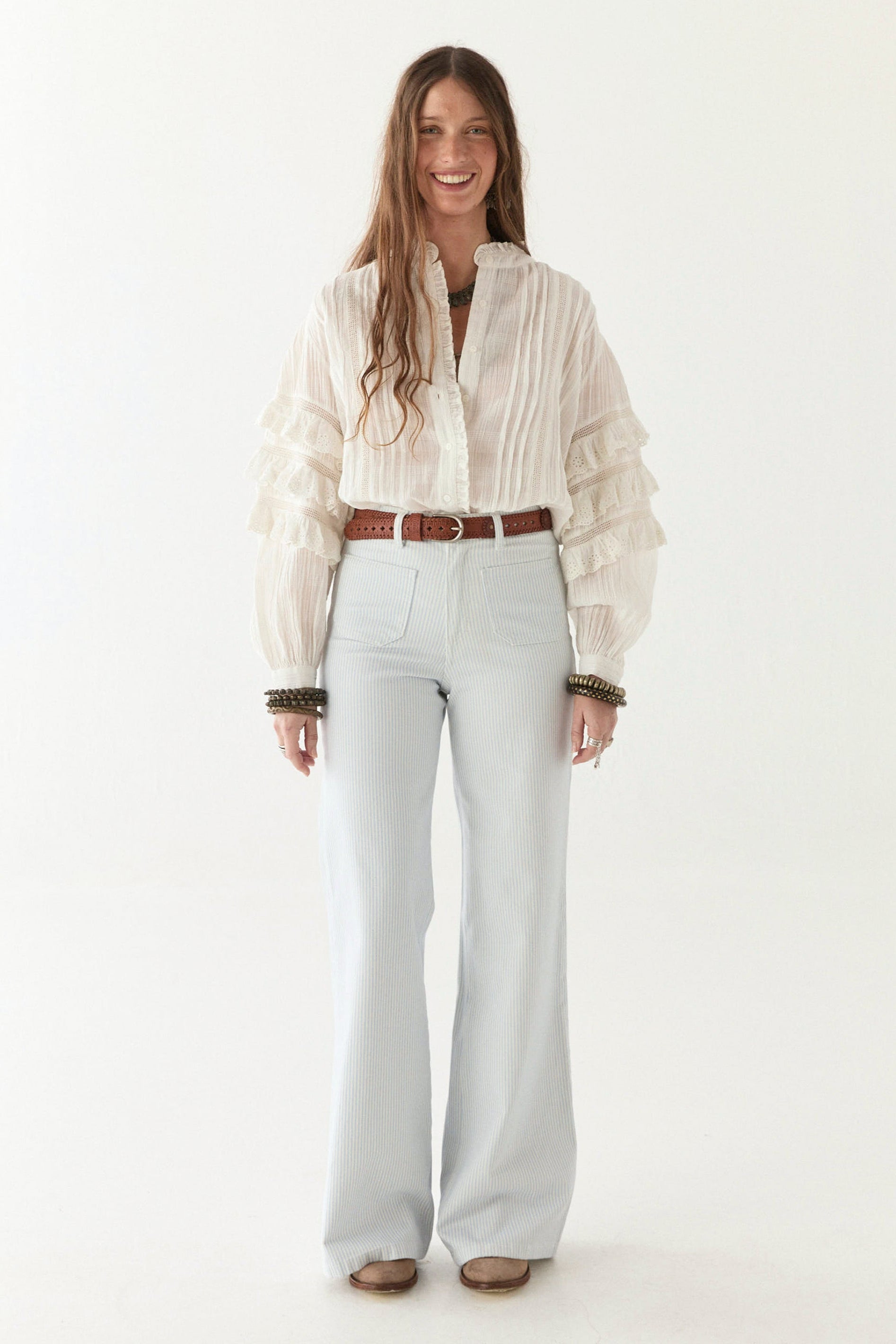 Womens flowy off white shirt with ruffled sleeves paired with white jeans and a tan belt.  