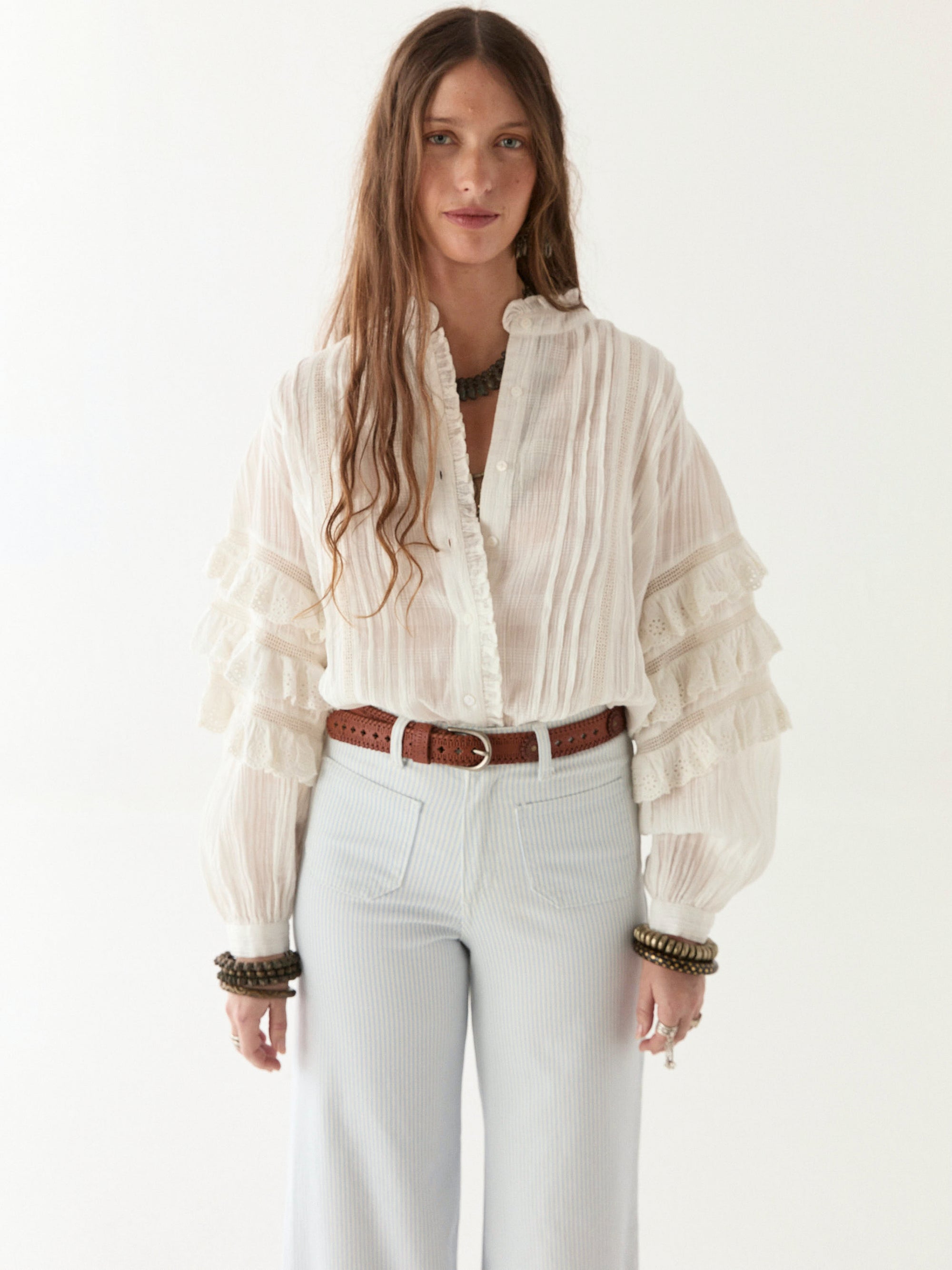 Womens flowy off white shirt paired with white jeans and a tan belt.  