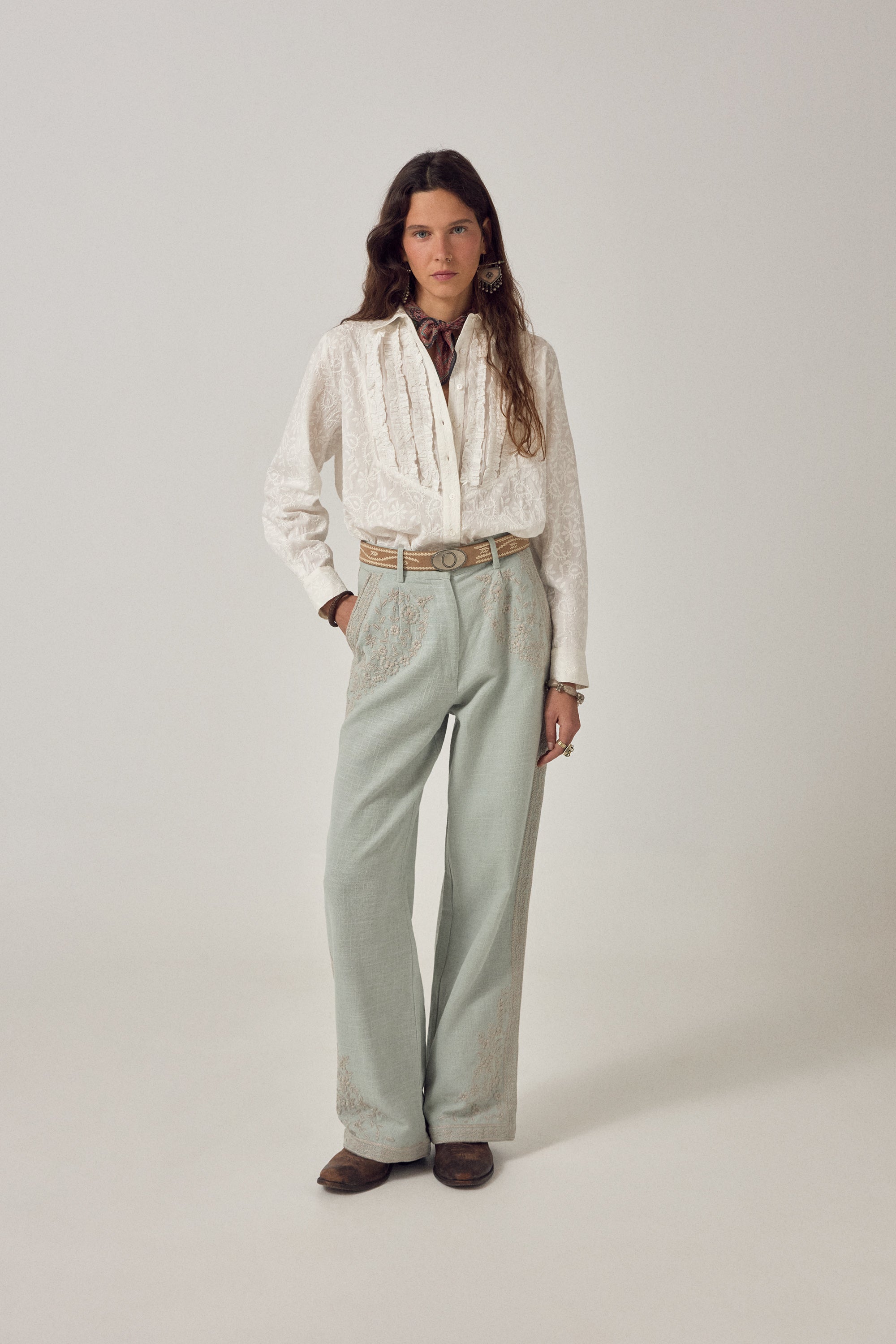 Woman wearing ecru long sleeve embroidered shirt with frill detail on a plain background. 