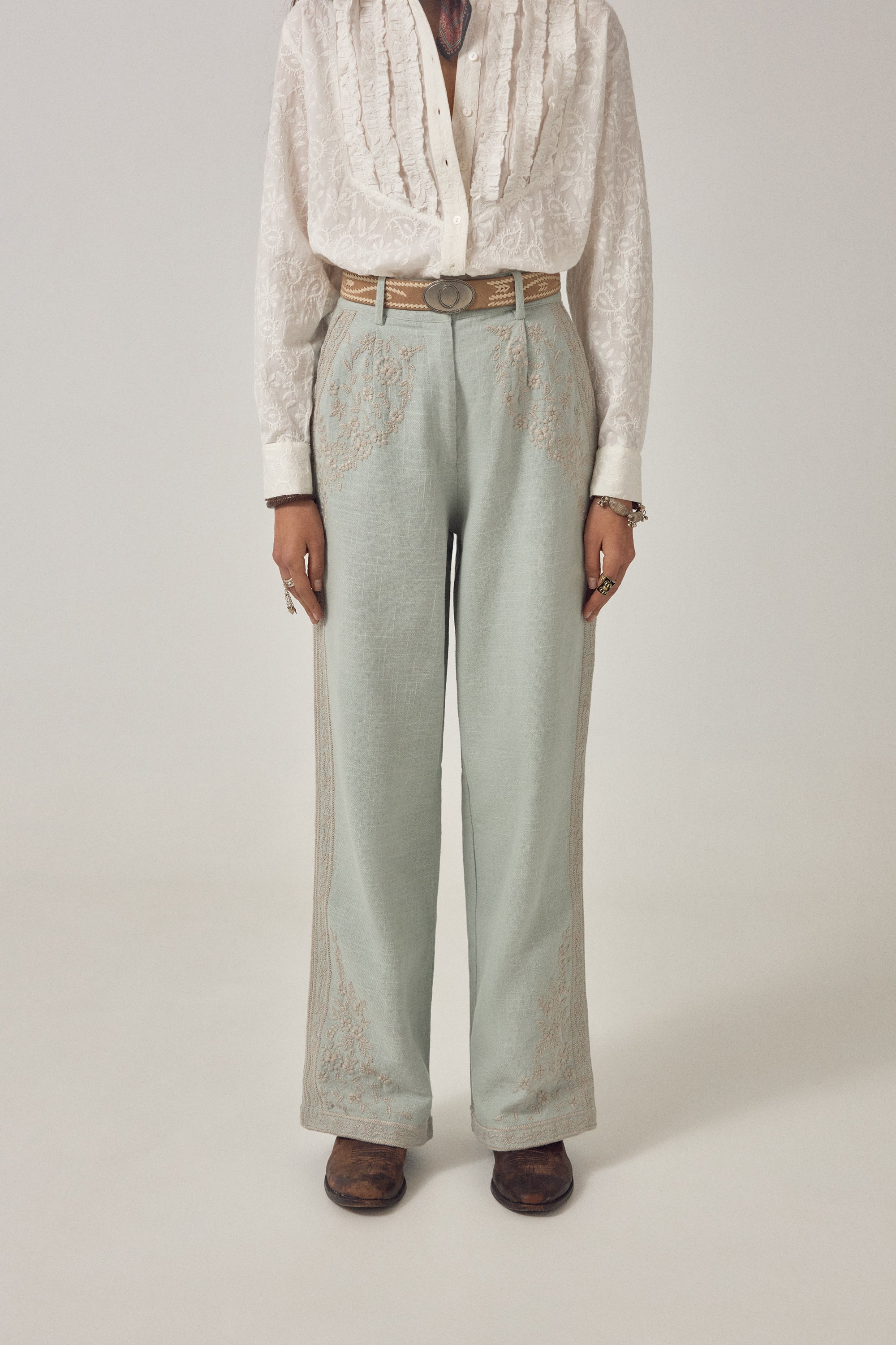 Woman wearing ecru long sleeve embroidered shirt with frill detail on a plain background. 