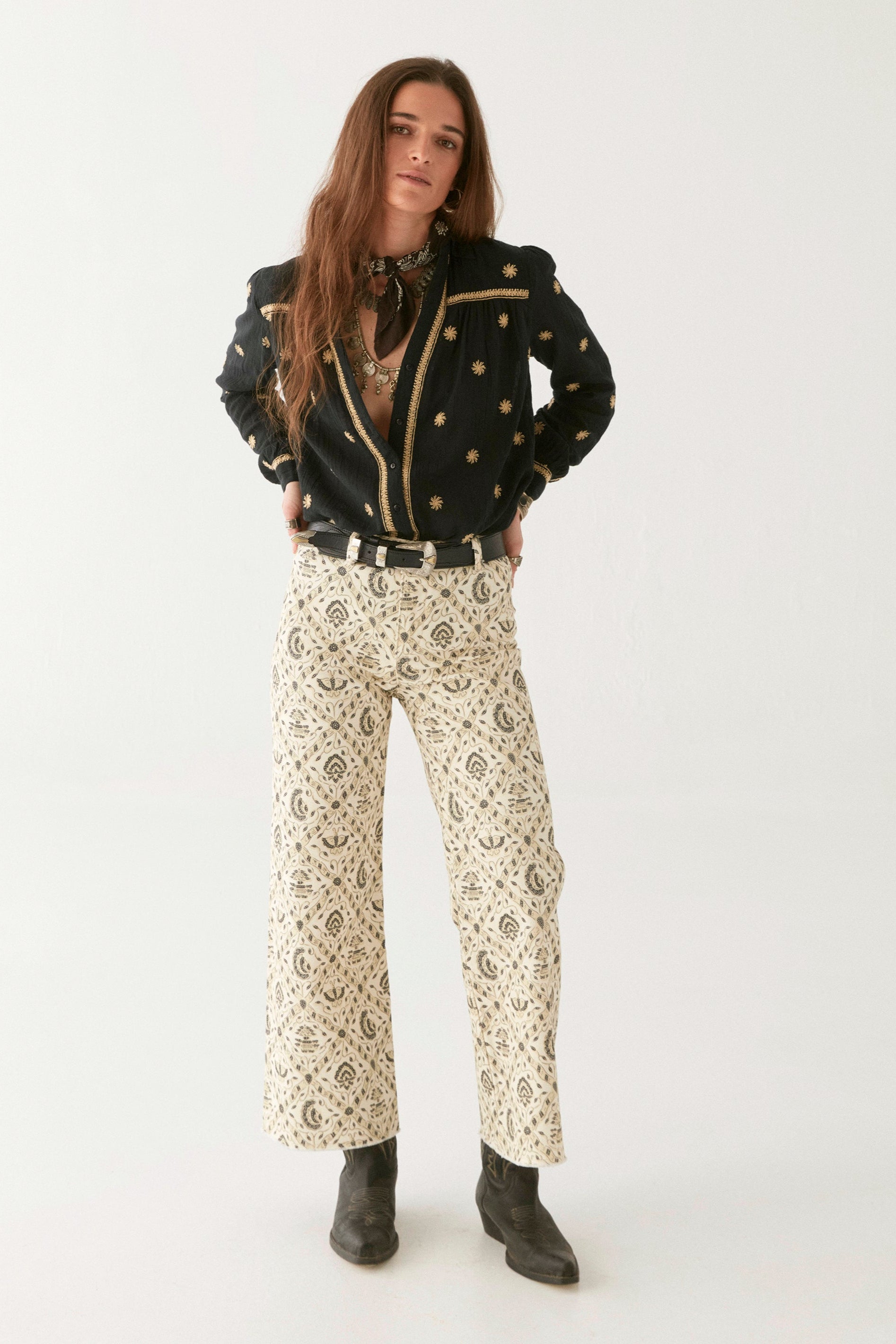 Model wearing black cotton blouse with gold embroidery. Paired with cream patterned trousers on a white background.  