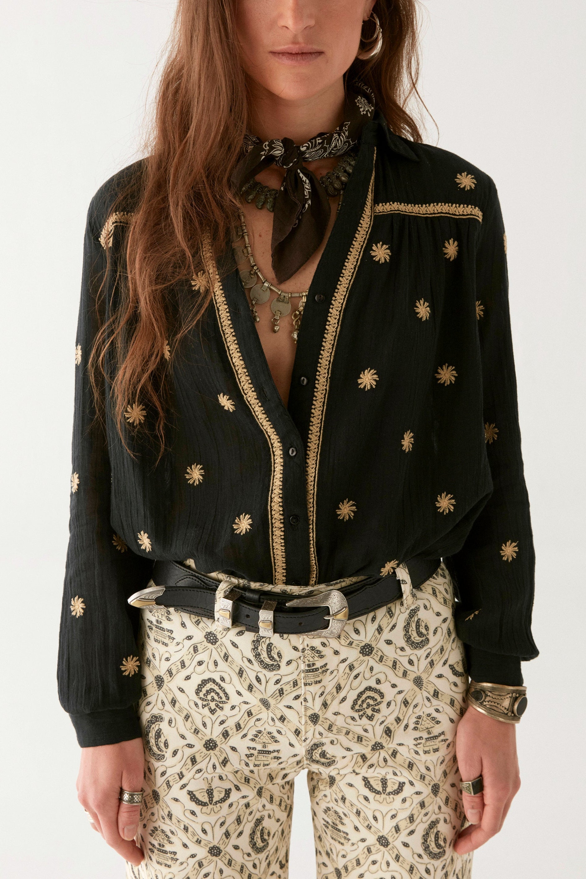Model wearing black cotton blouse with gold embroidery. Paired with cream patterned trousers on a white background.  