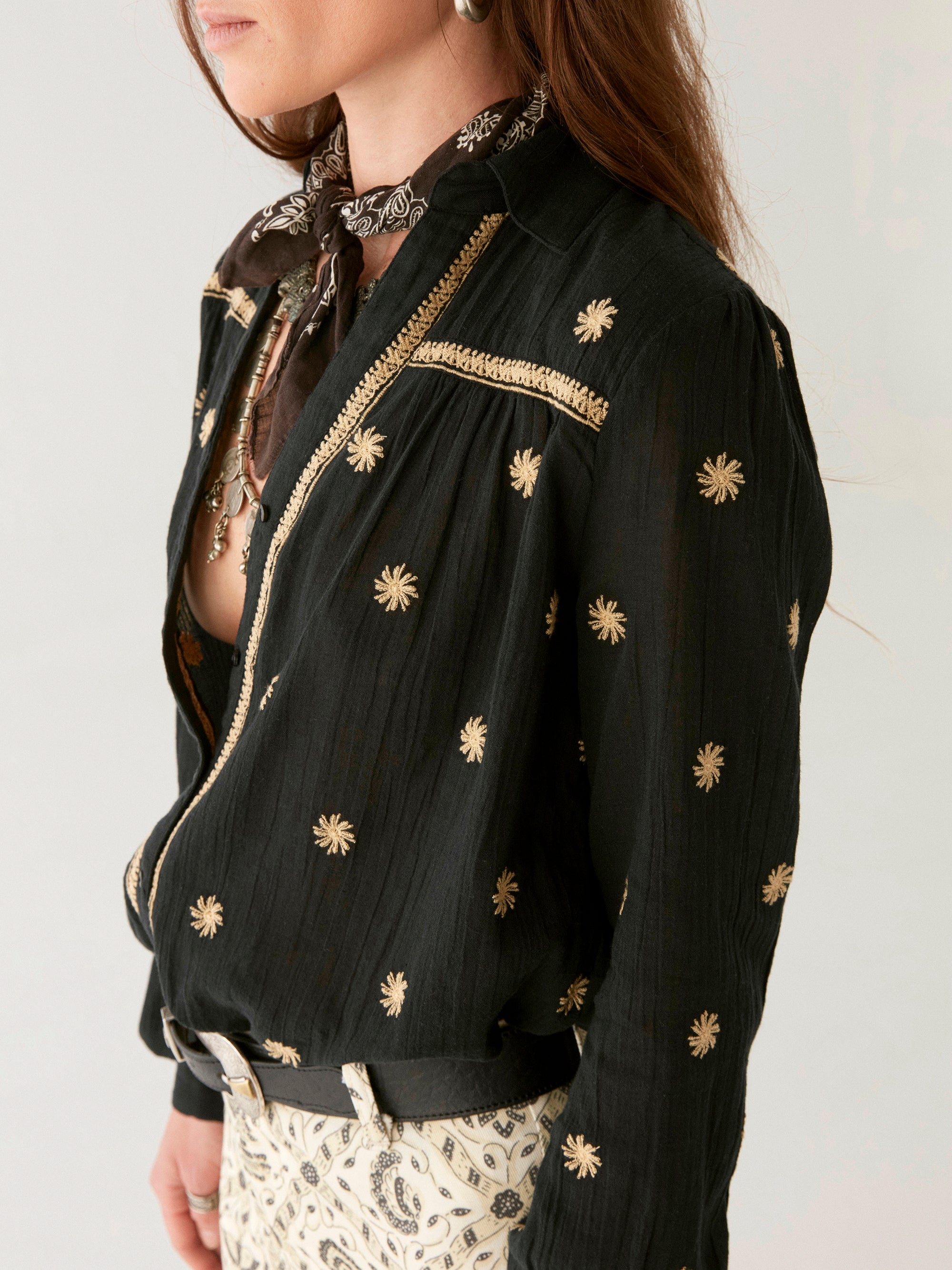 Model wearing black cotton blouse with gold embroidery. Paired with cream patterned trousers on a white background.  