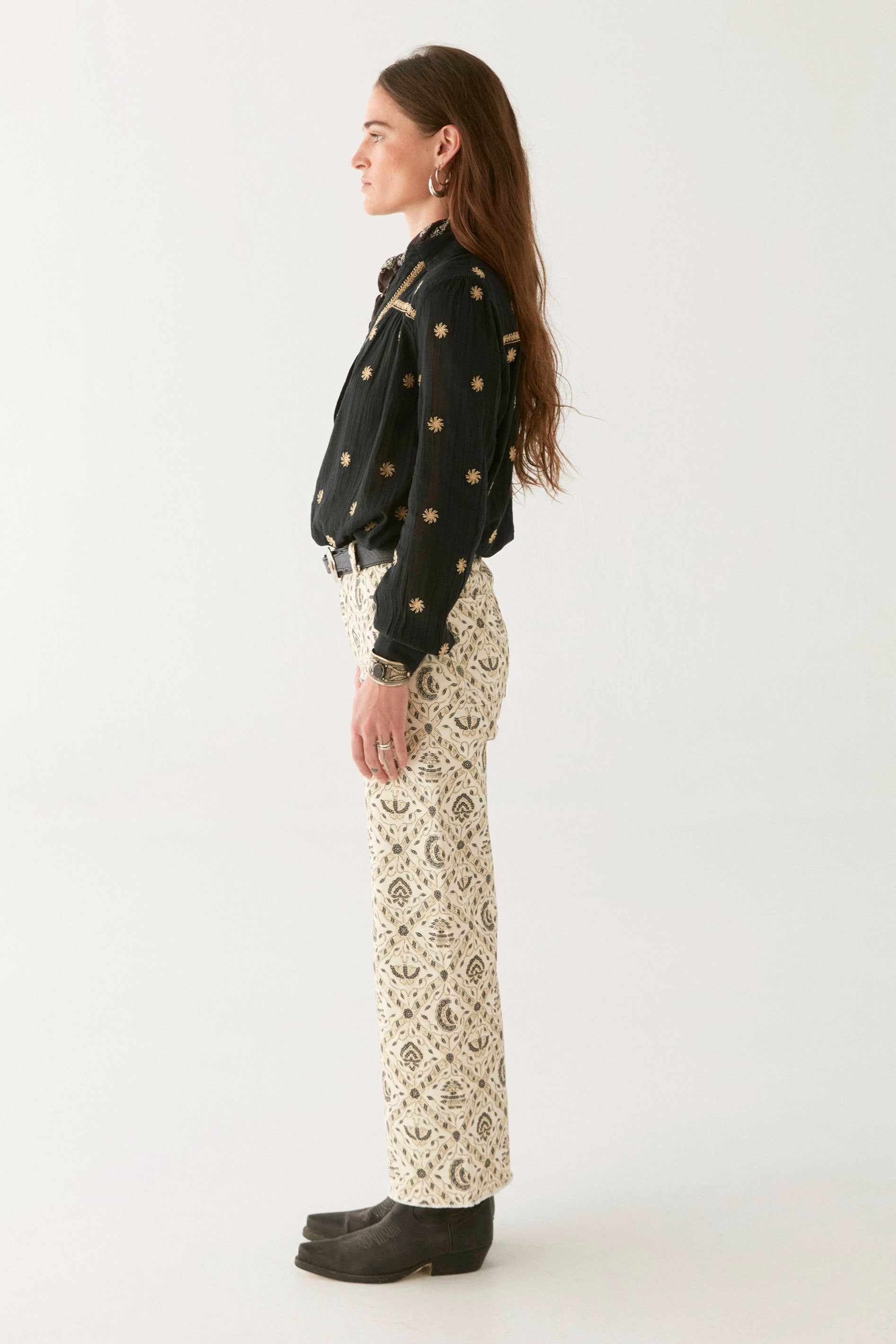 Model wearing black cotton blouse with gold embroidery. Paired with cream patterned trousers on a white background.  