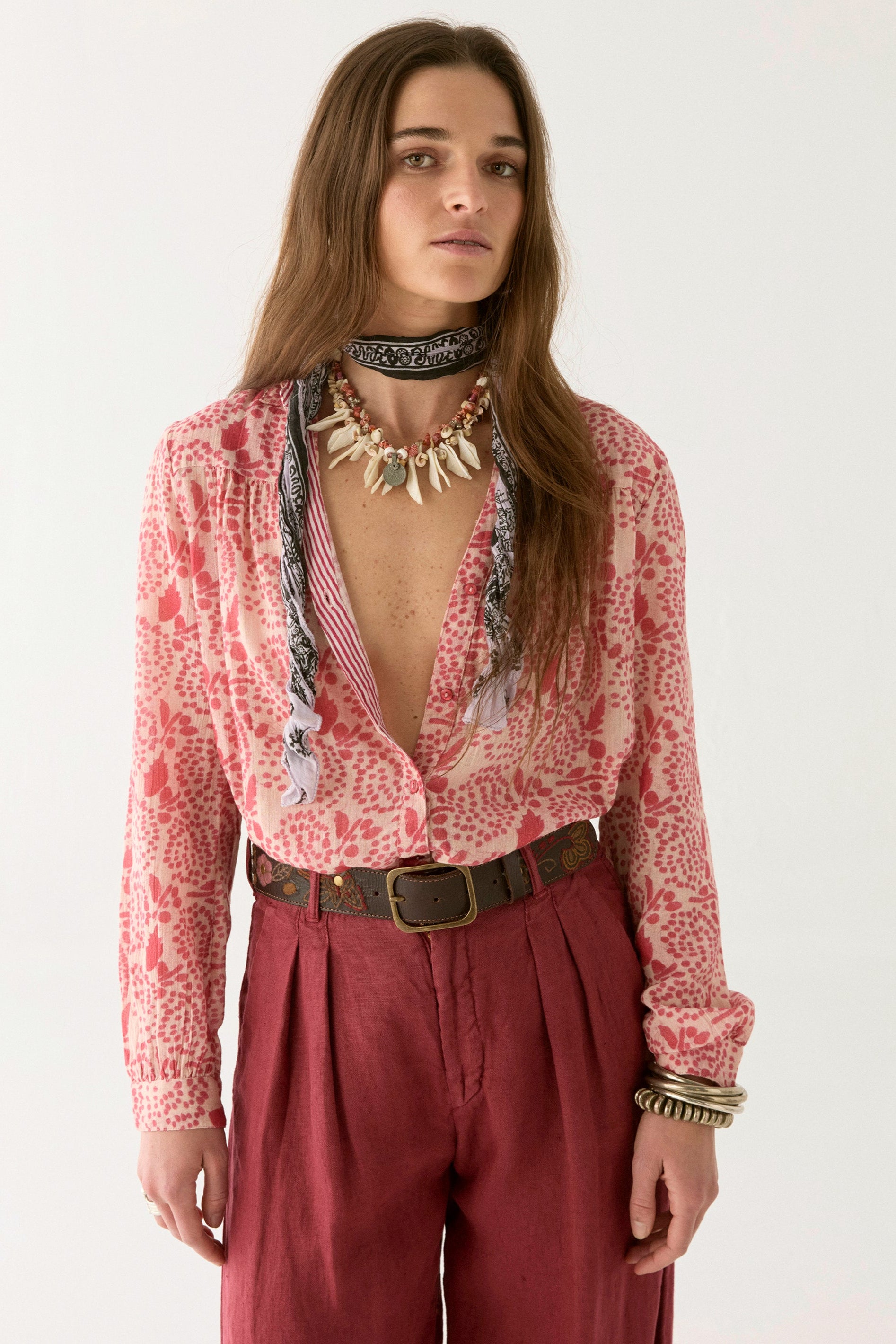 Pink and white floral blouse with open collar paired with pink pants and a tan belt woman up close. 