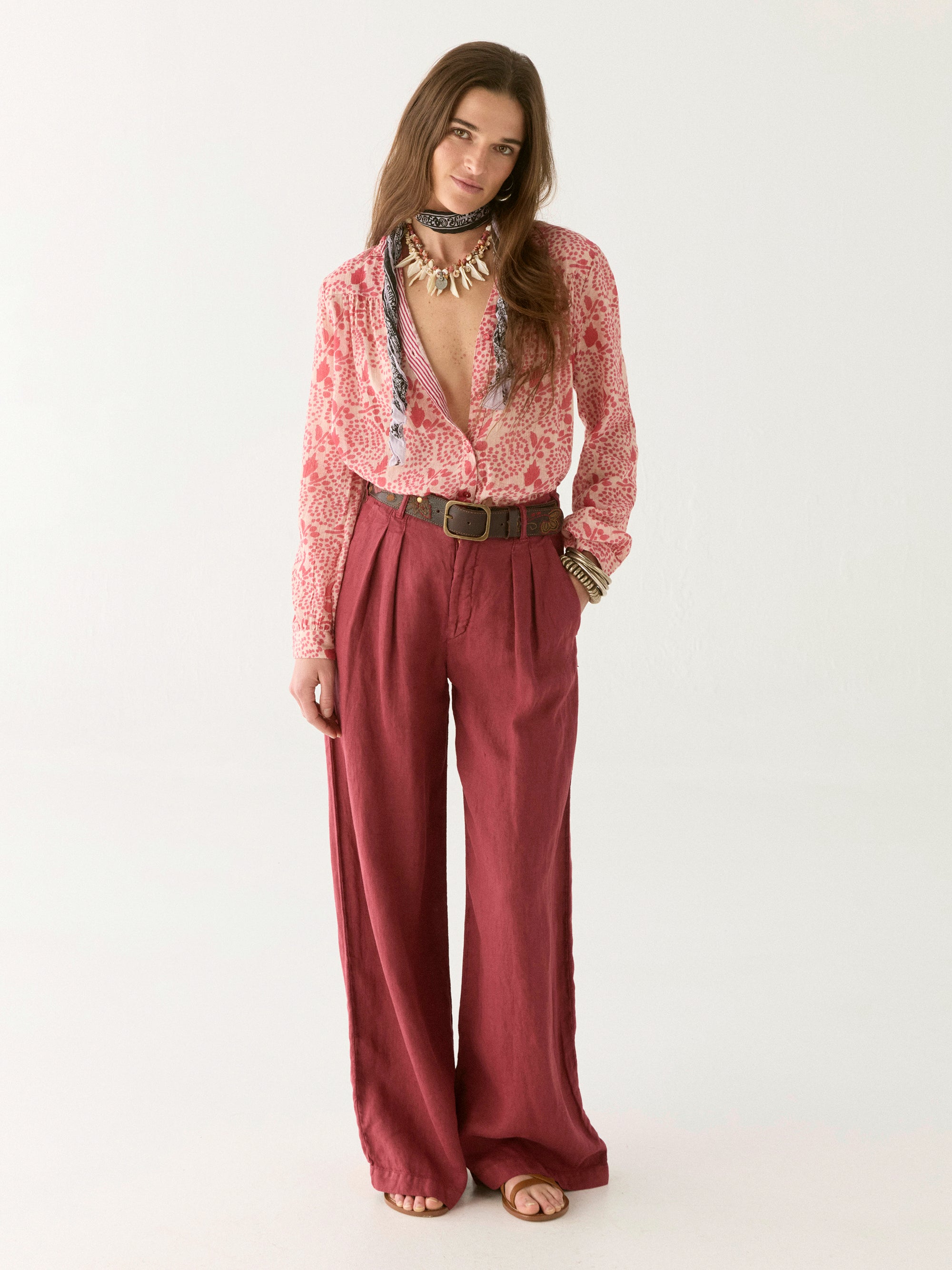 Pink and white floral blouse with open collar paired with pink pants and a tan belt. 
