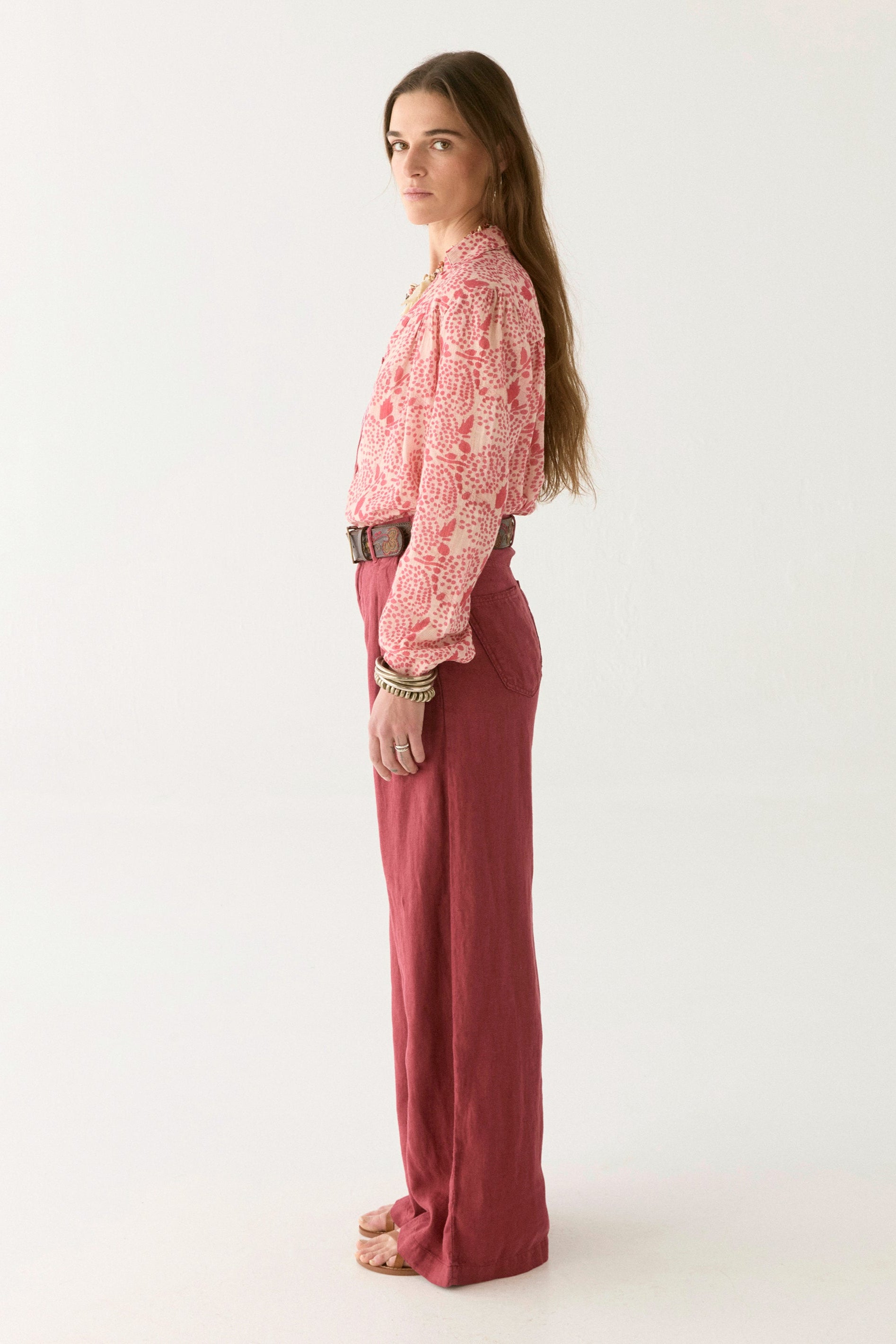 Pink and white floral blouse with open collar paired with pink pants and a tan belt. 