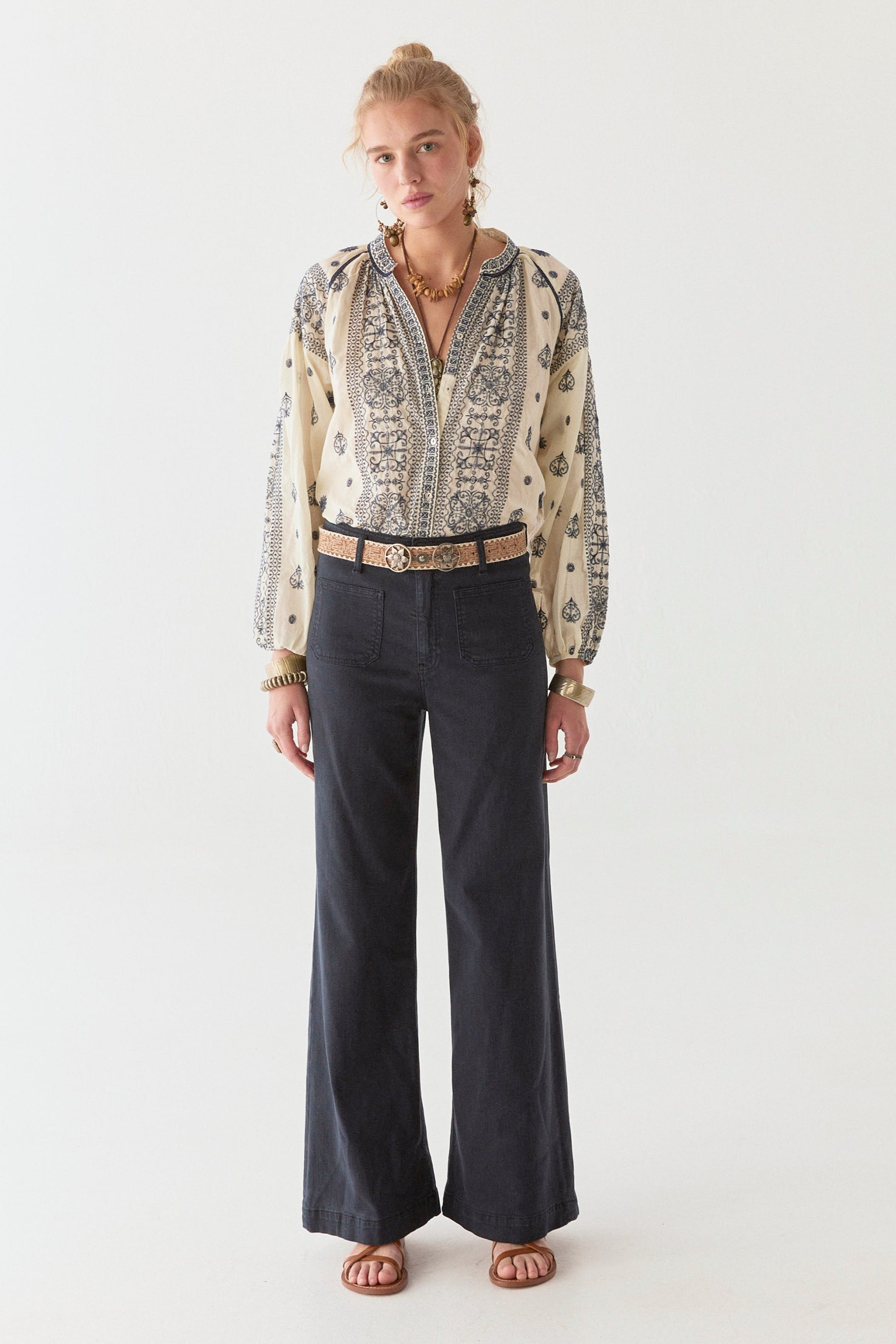 Model wearing navy wide leg pant and cream and navy cotton blouse on a white background.  Paired with tan sandals. 