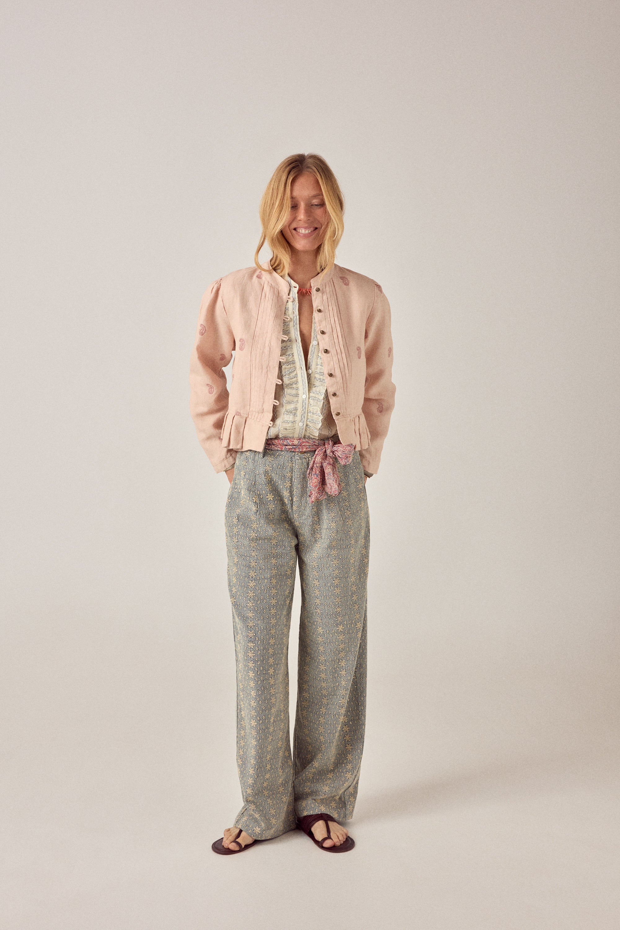 Woman wearing a beige patterned shirt with a pink jacket on a plain background