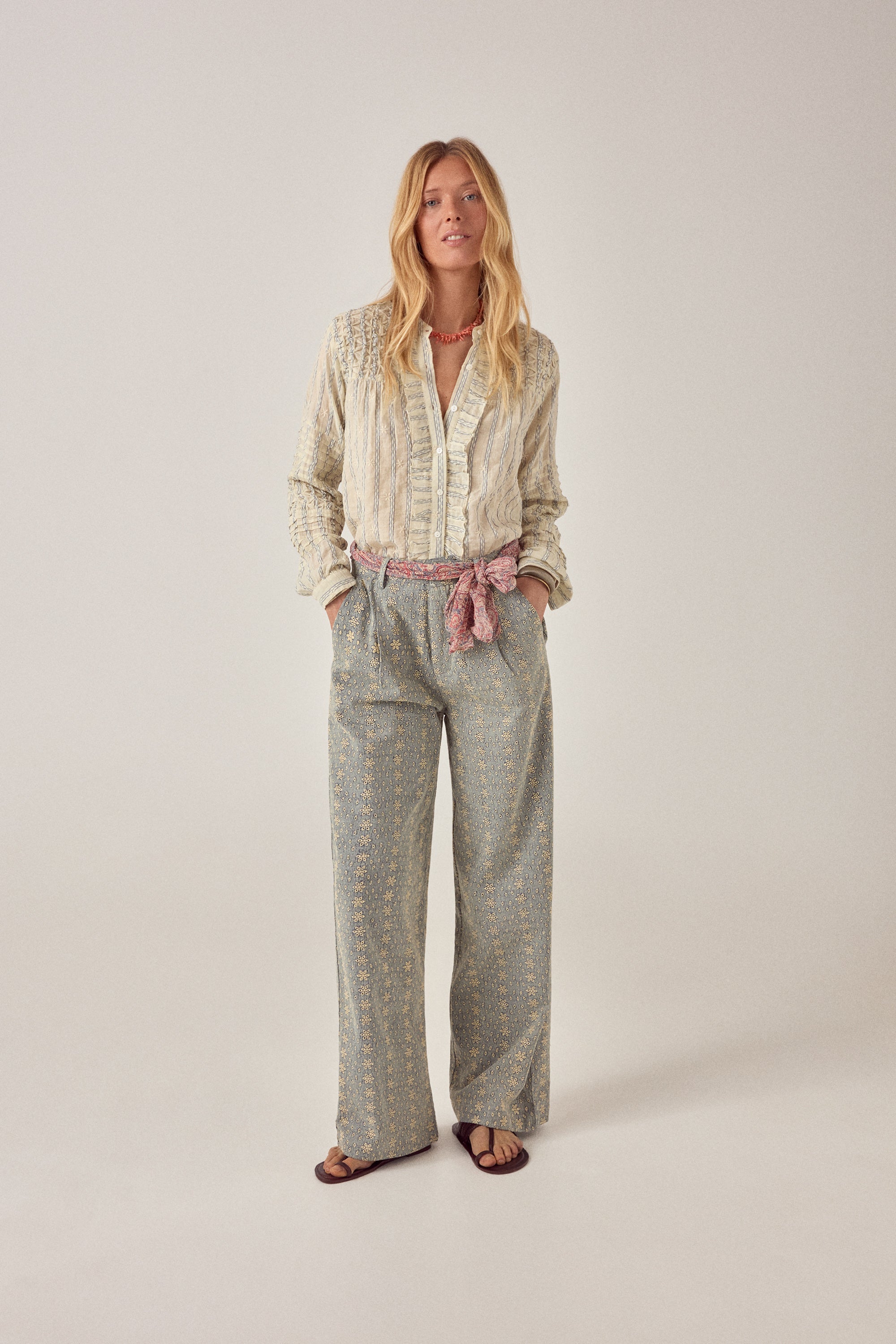 Woman wearing a patterned shirt and pants on a plain background