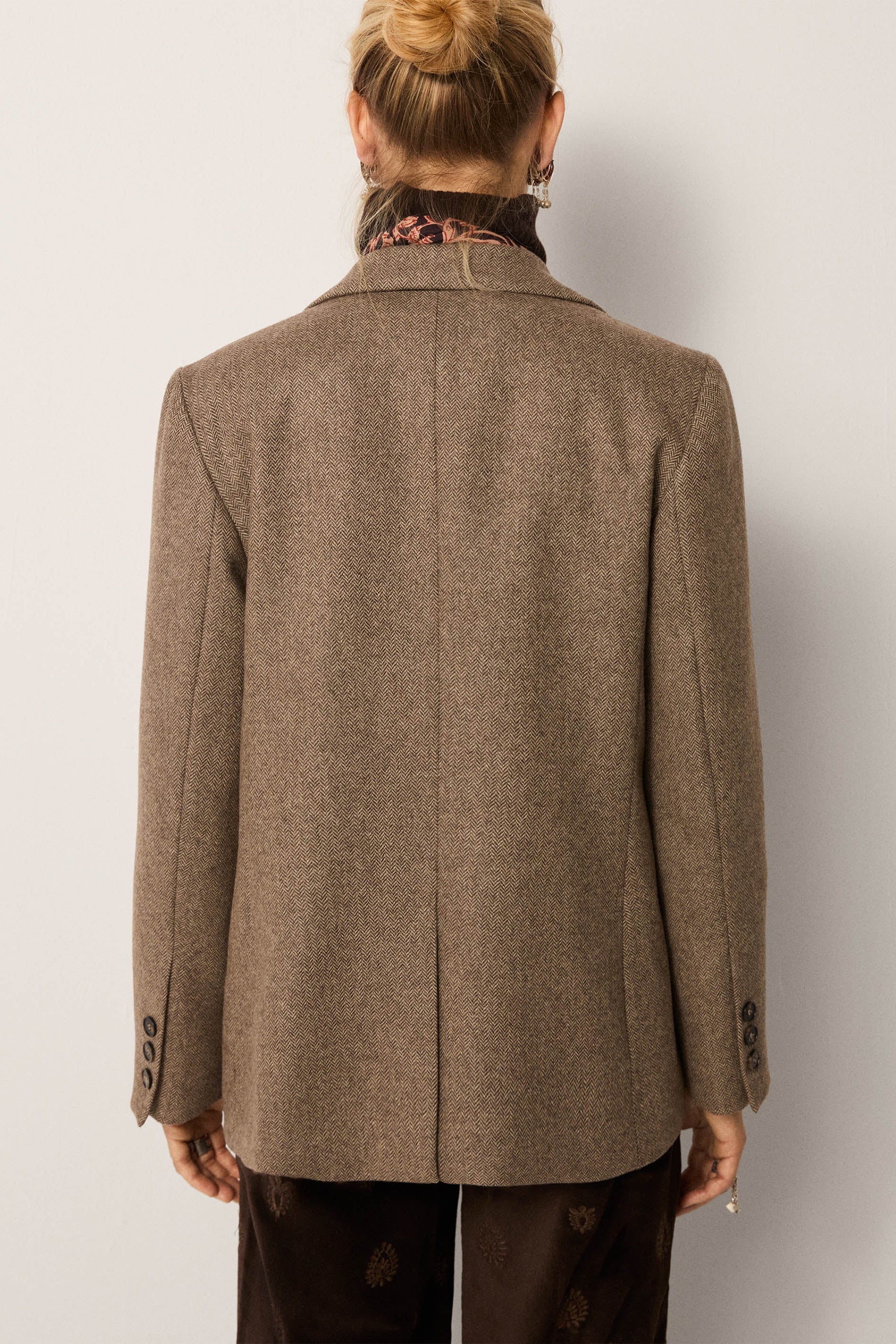 Person wearing a brown coat from behind on a plain background