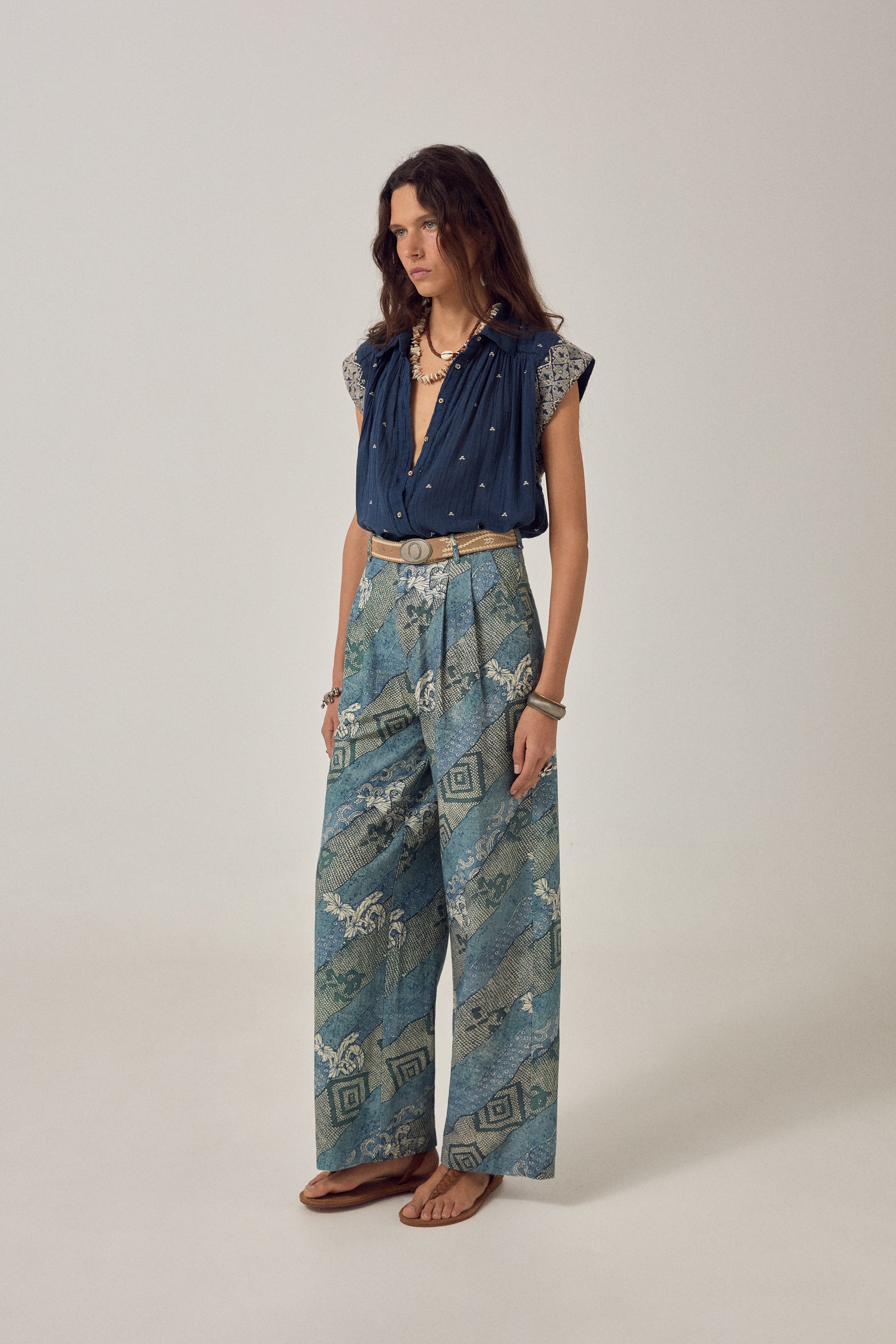 Woman wearing a blue embroidered top and patterned skirt against a plain background