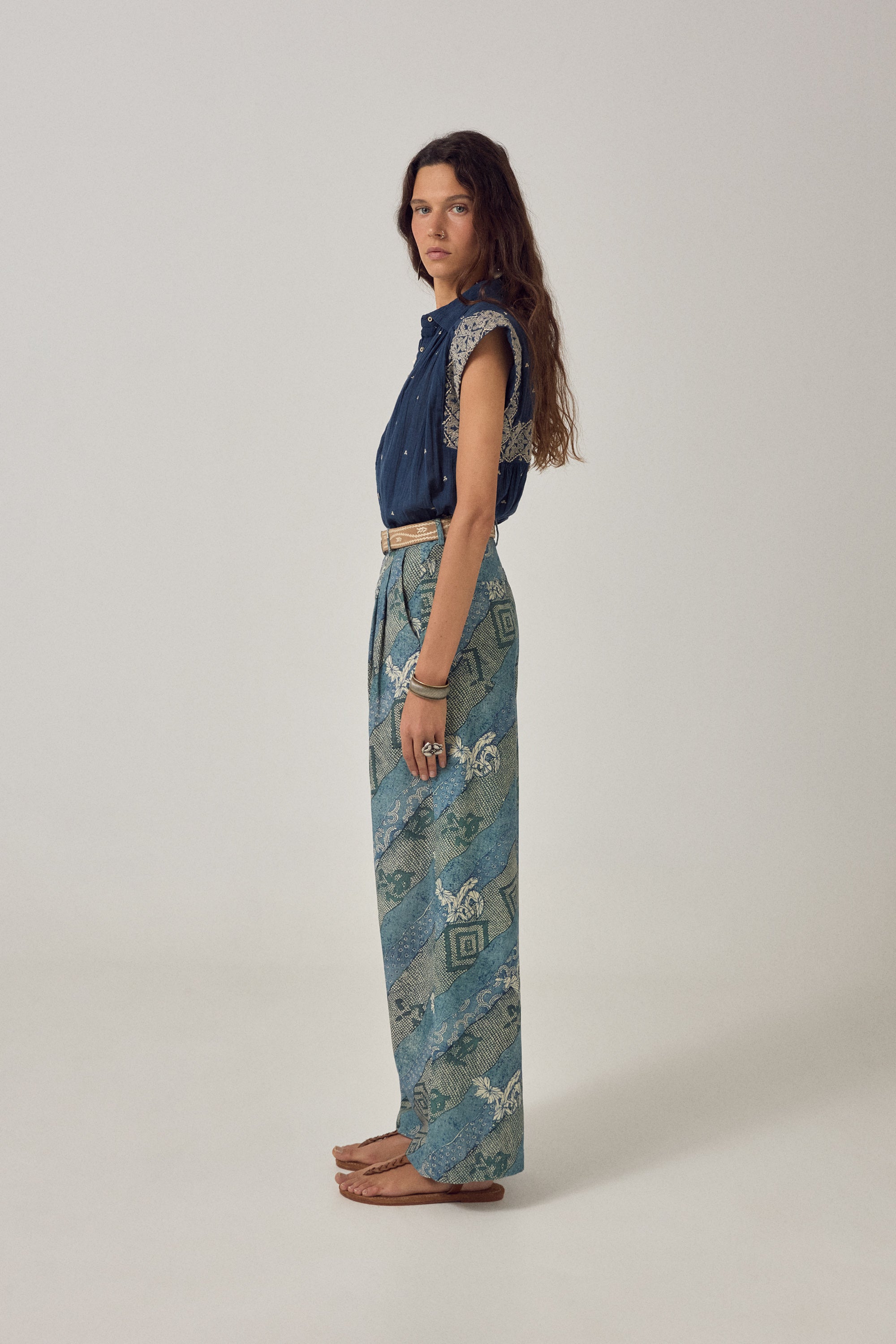 Woman wearing a blue embroidered top and patterned skirt against a plain background