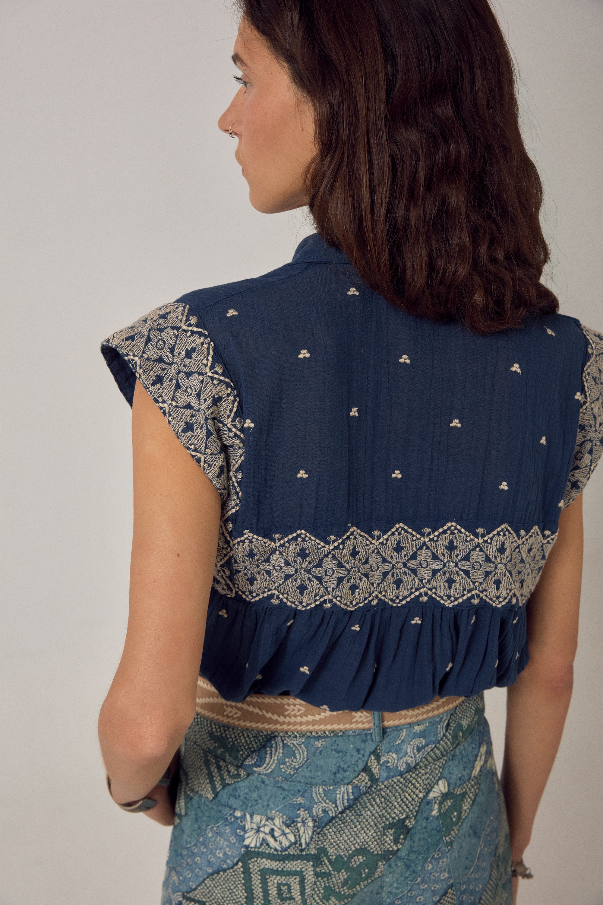 Woman wearing a blue embroidered top and patterned skirt against a plain background