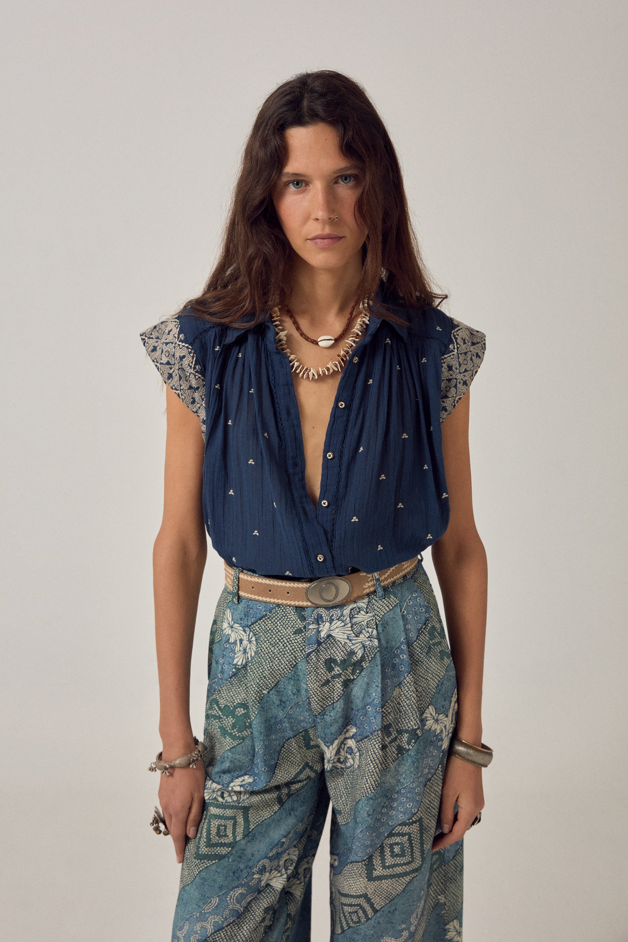 Woman wearing a blue embroidered top and patterned skirt against a plain background