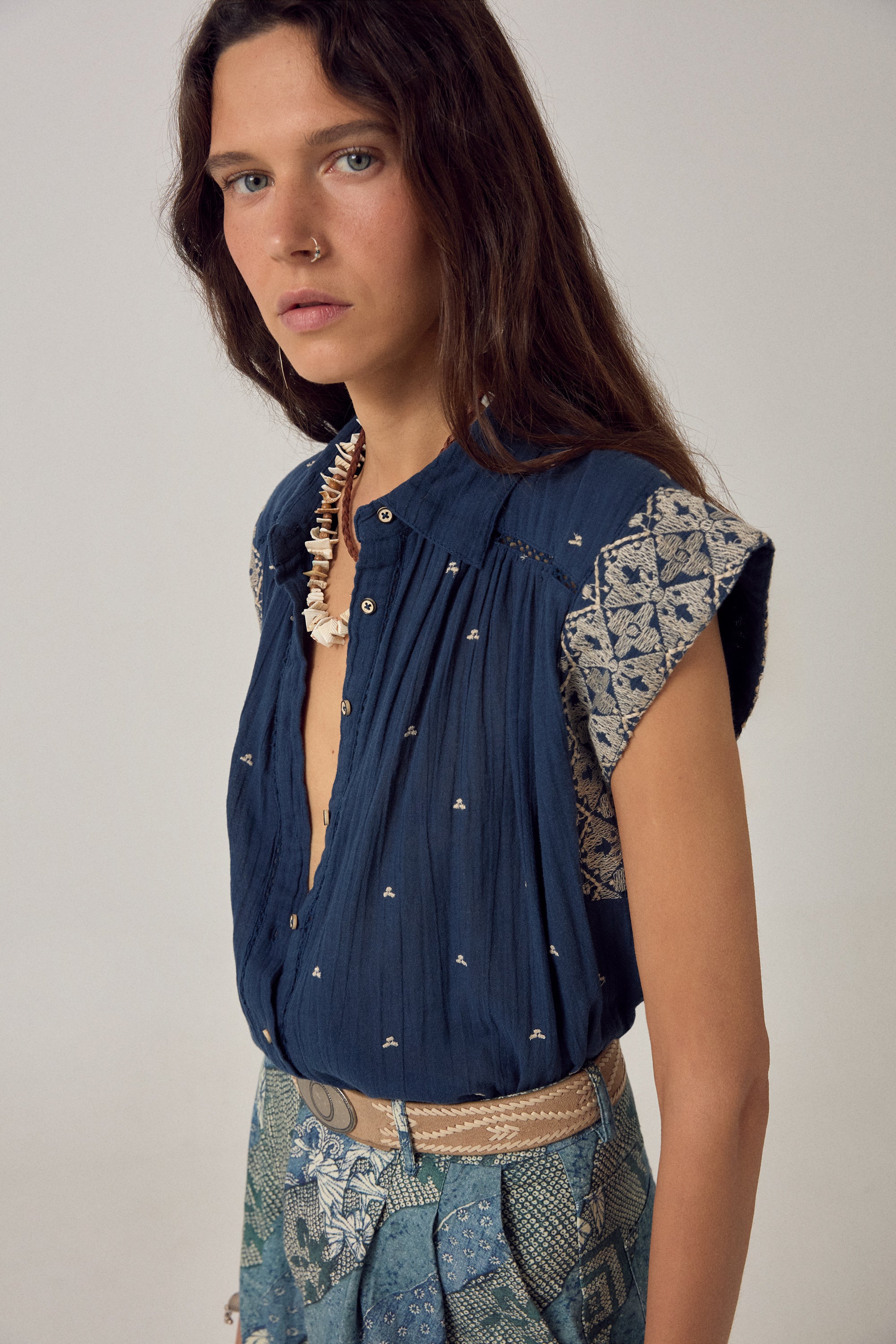 Woman wearing a blue embroidered top and patterned skirt against a plain background