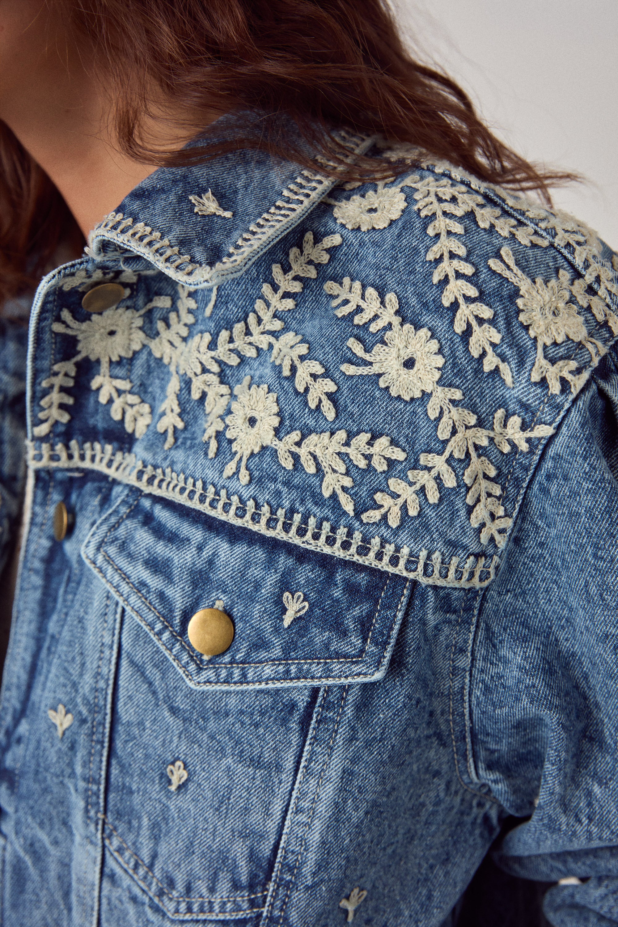 Denim jacket with intricate white embroidery on a plain background