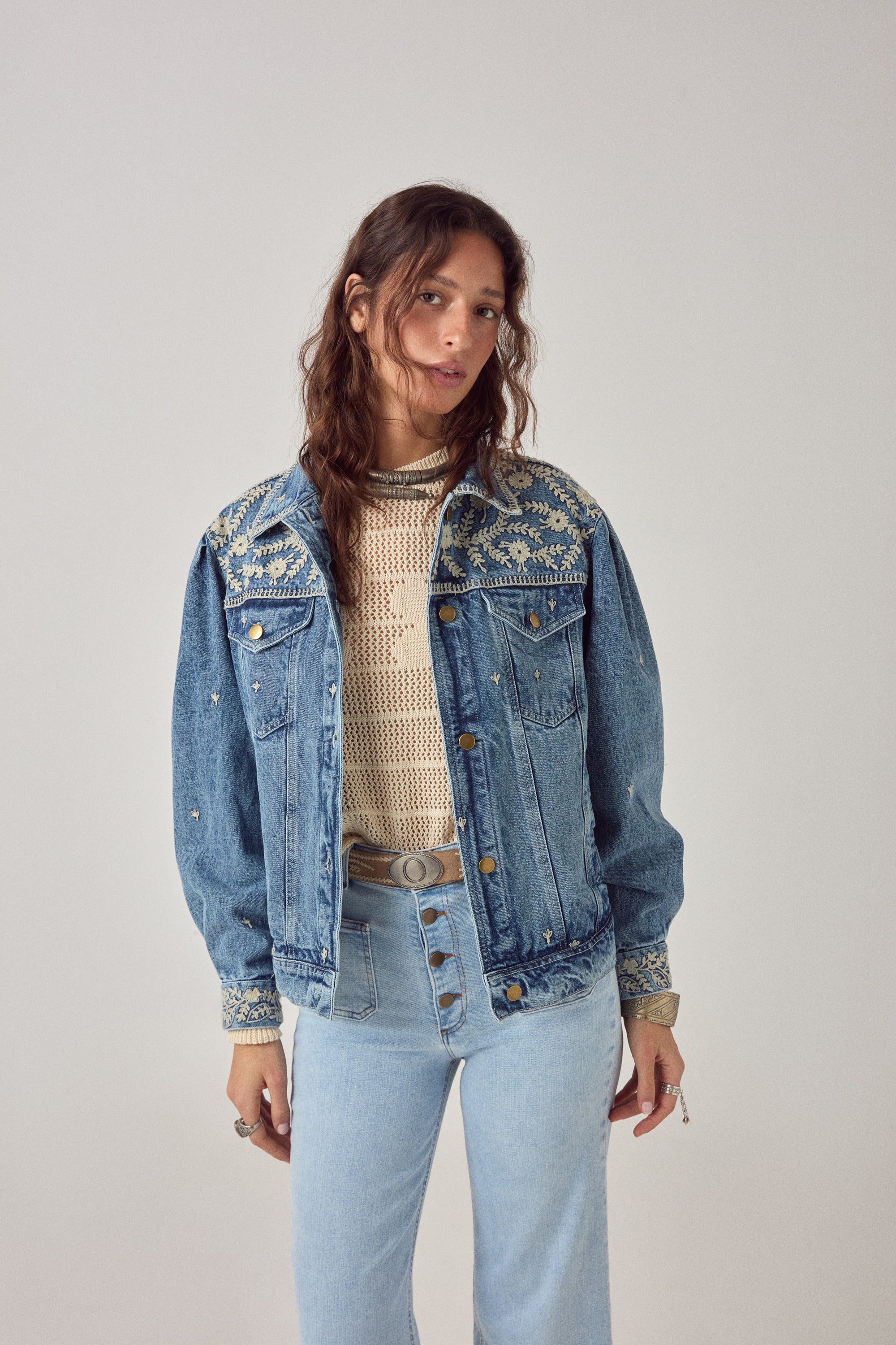 Woman wearing a denim jacket and light blue jeans on a plain background