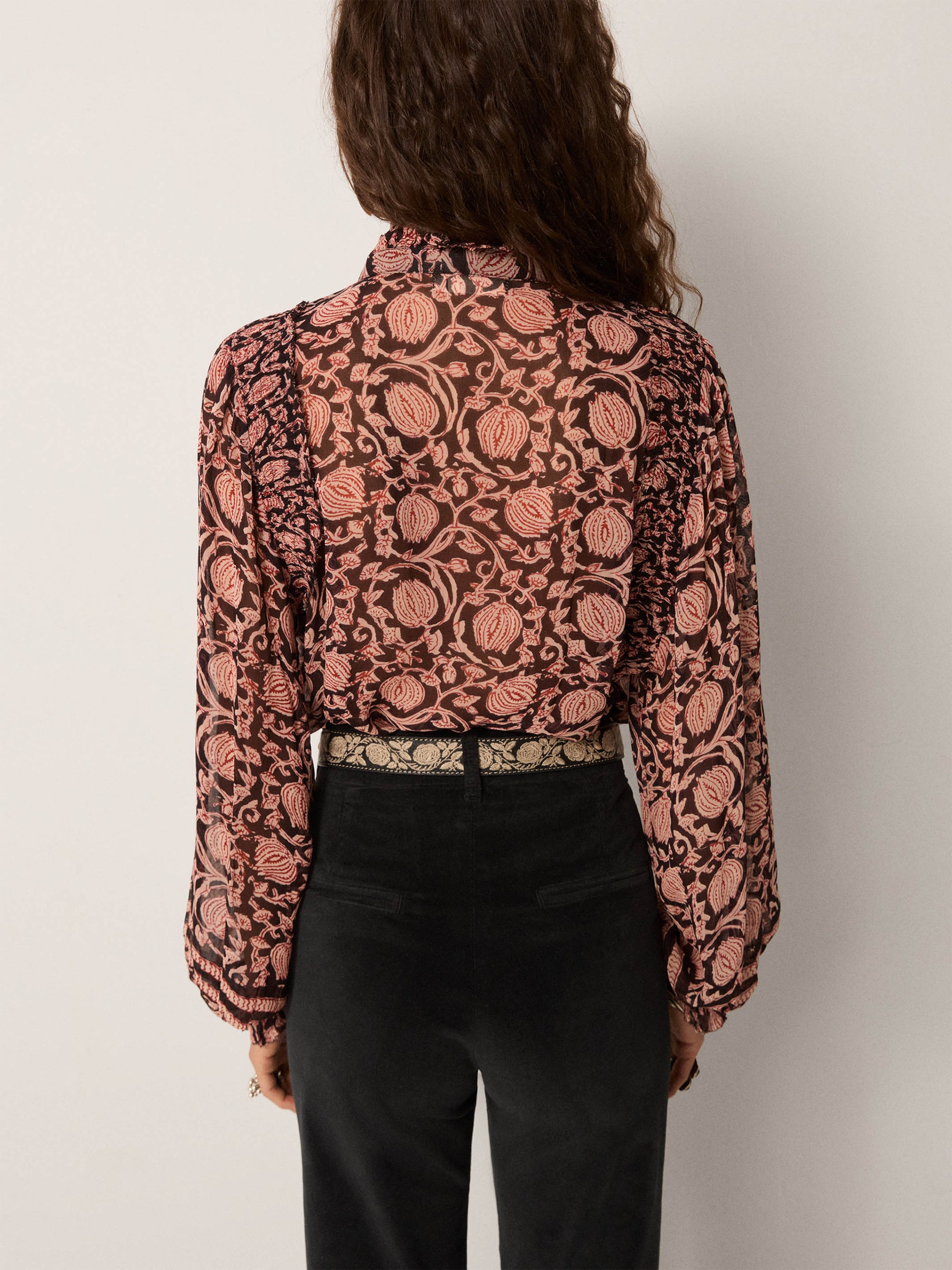 Person wearing a patterned blouse with long sleeves against a plain background