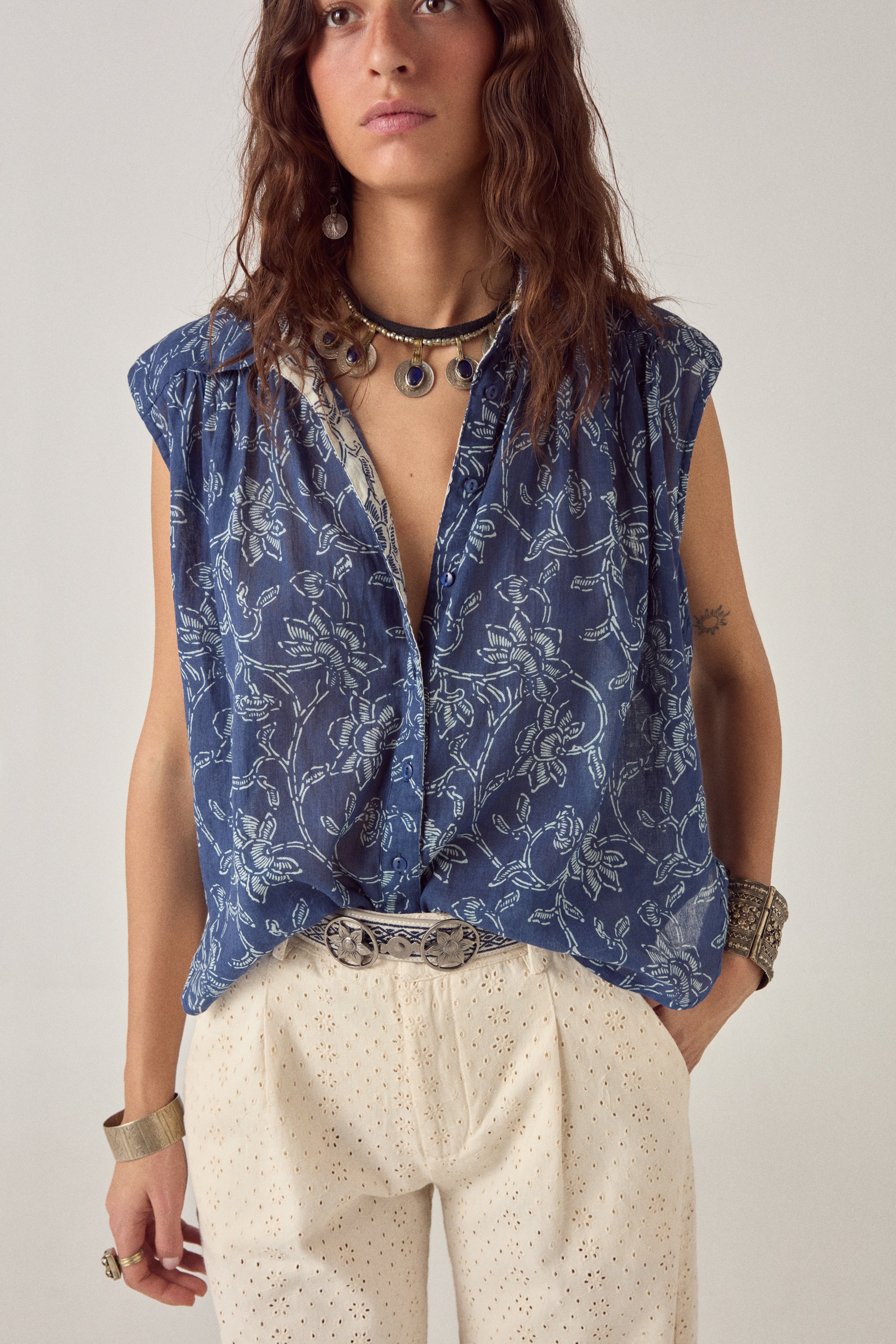 Woman wearing a blue sleeveless floral blouse with a plain background