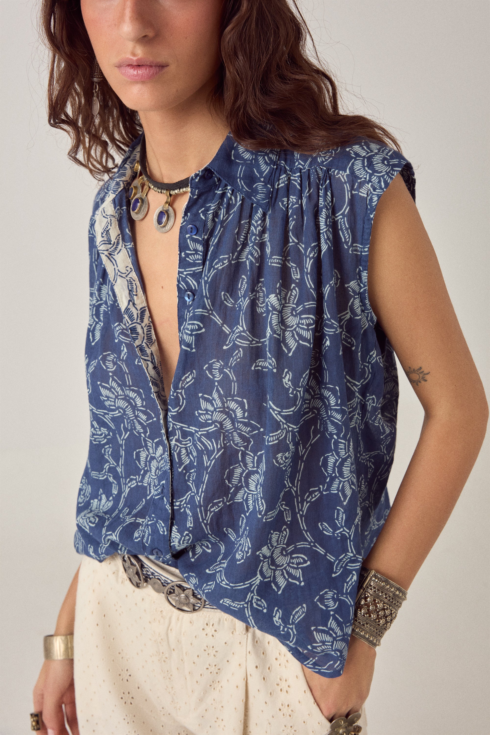 Woman wearing a blue sleeveless floral blouse with a plain background