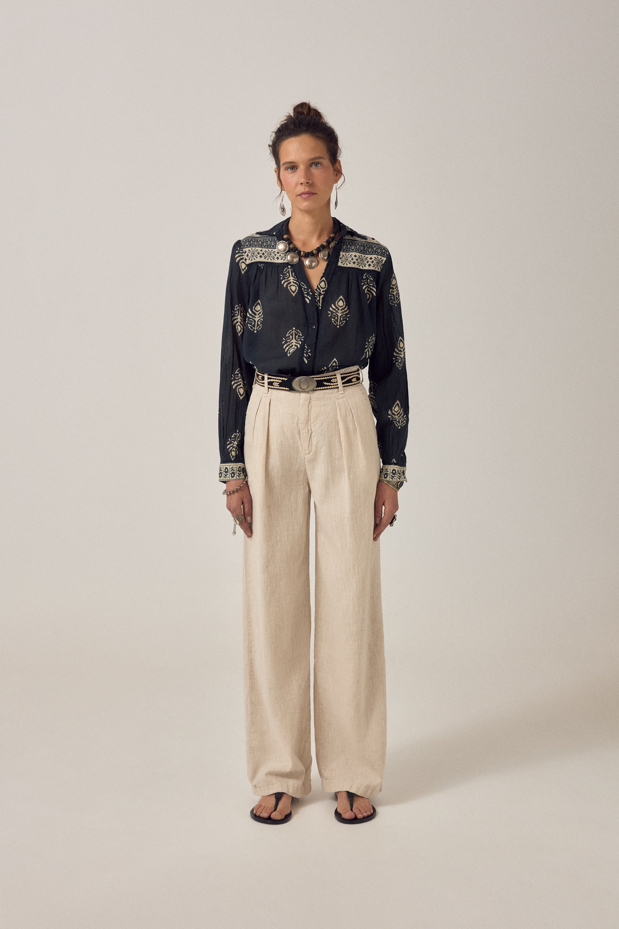 Woman wearing a black embroidered blouse with beige pants on a plain background