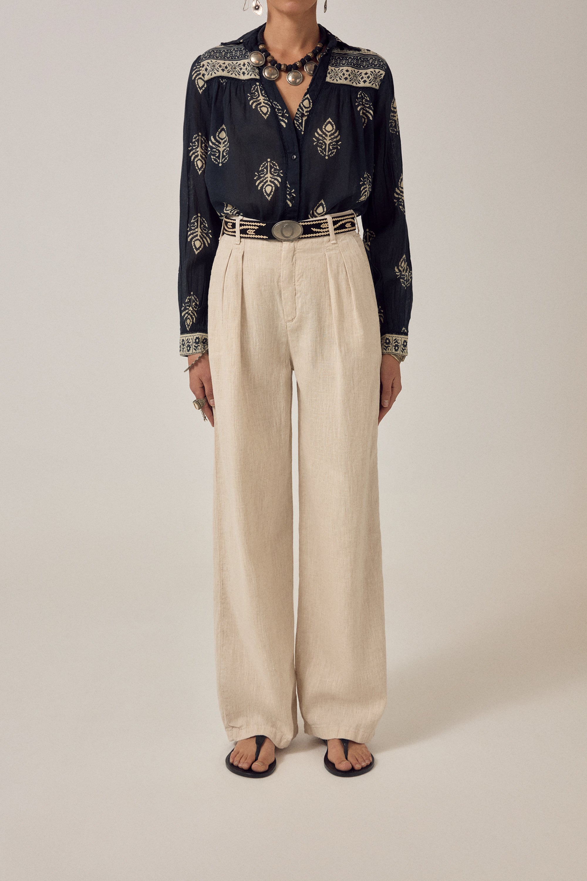 Woman wearing a black embroidered blouse with beige pants on a plain background