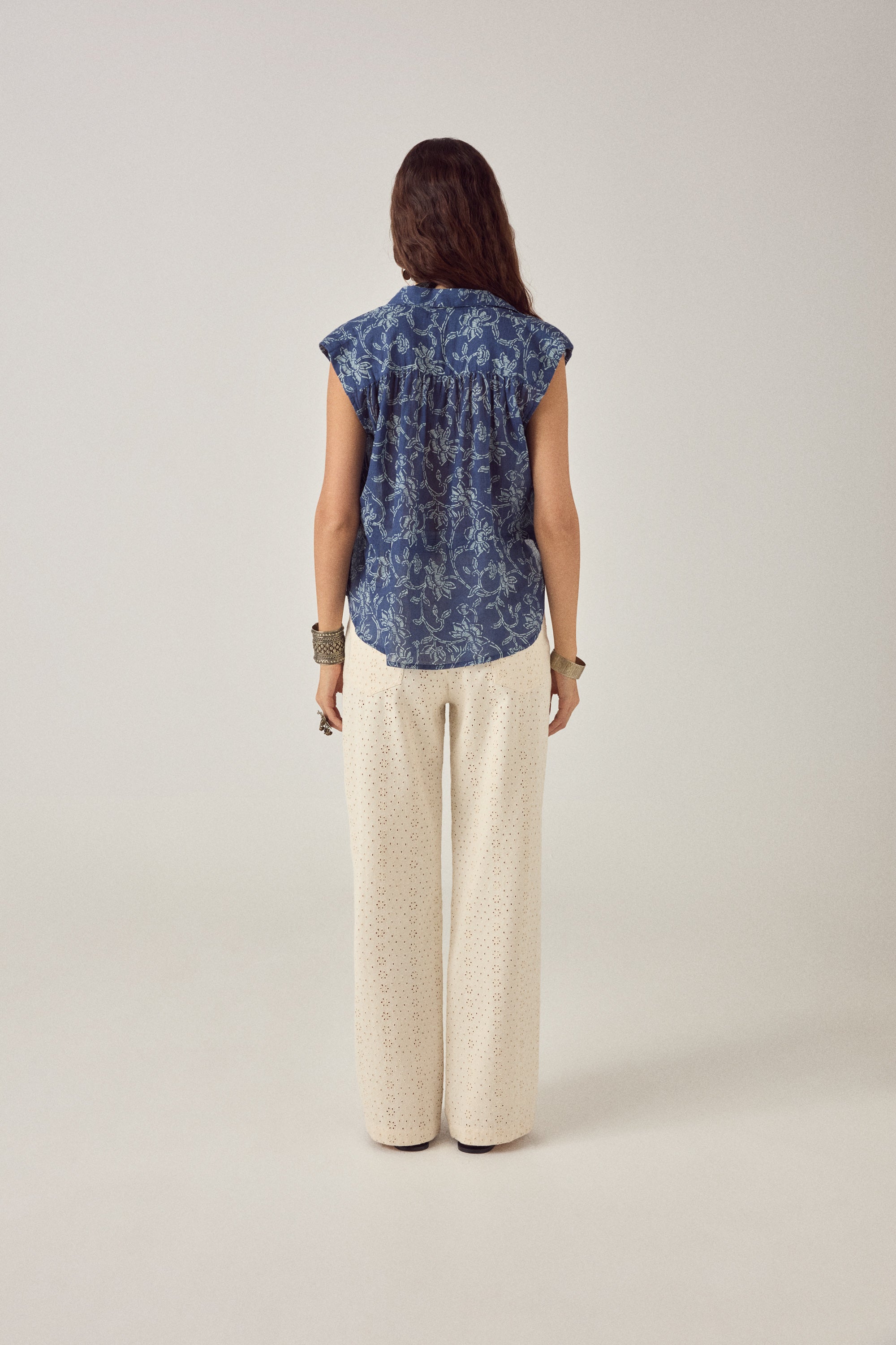 Woman wearing a blue sleeveless floral blouse with a plain background