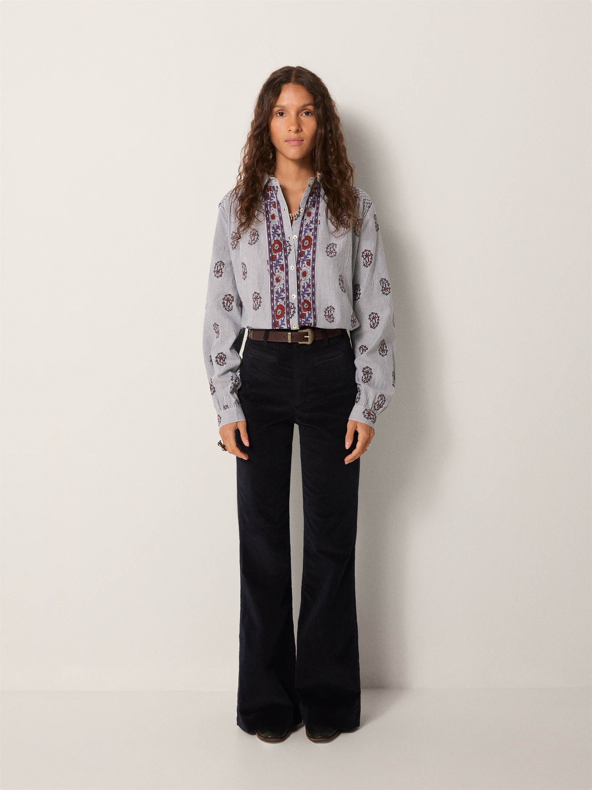 Person wearing a patterned blouse and black pants on a white background