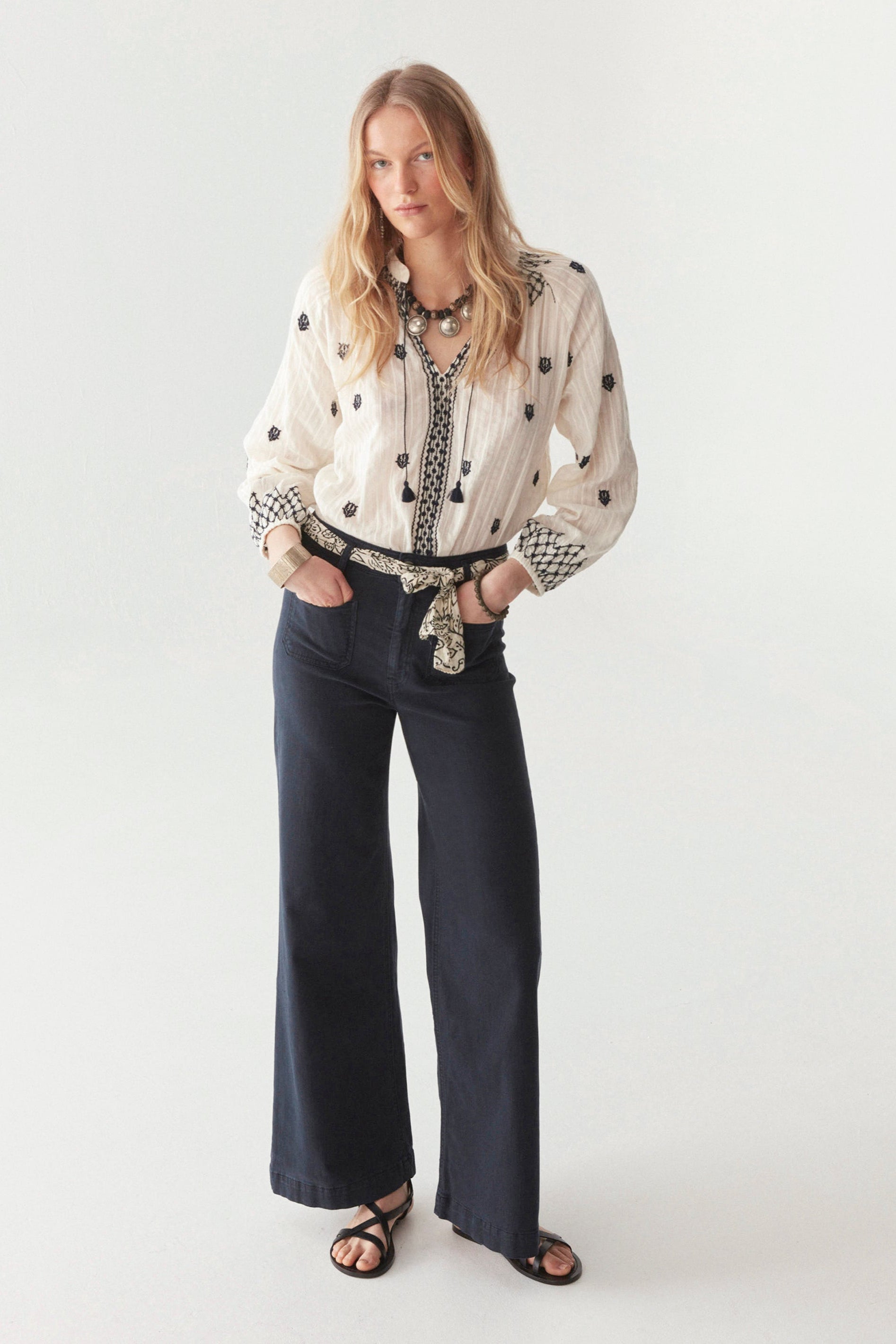 White cotton blouse with smocked neckline and navy embroidery all over with front tassels on model.  