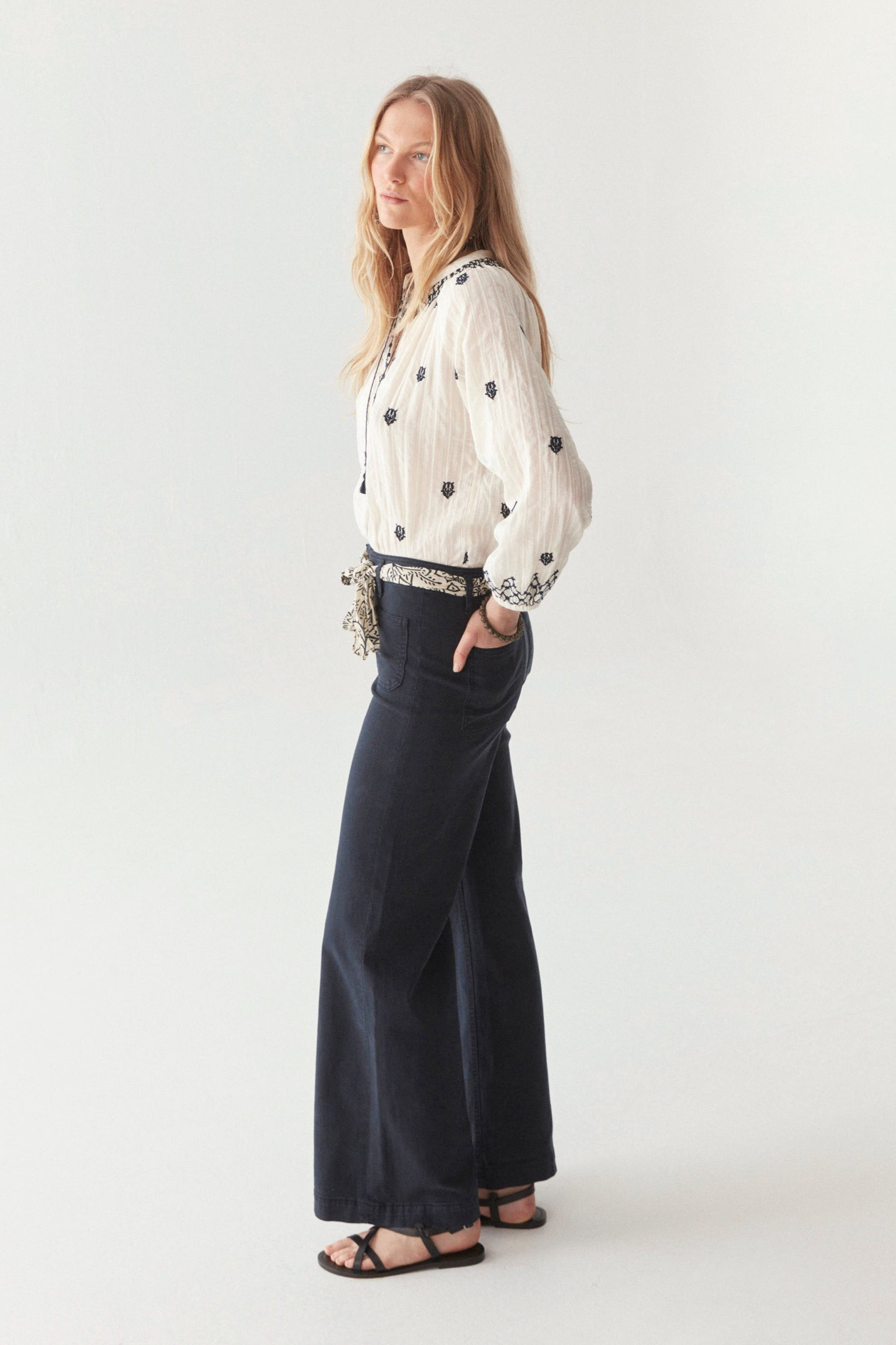 White cotton blouse with smocked neckline and navy embroidery all over with front tassels on model.  