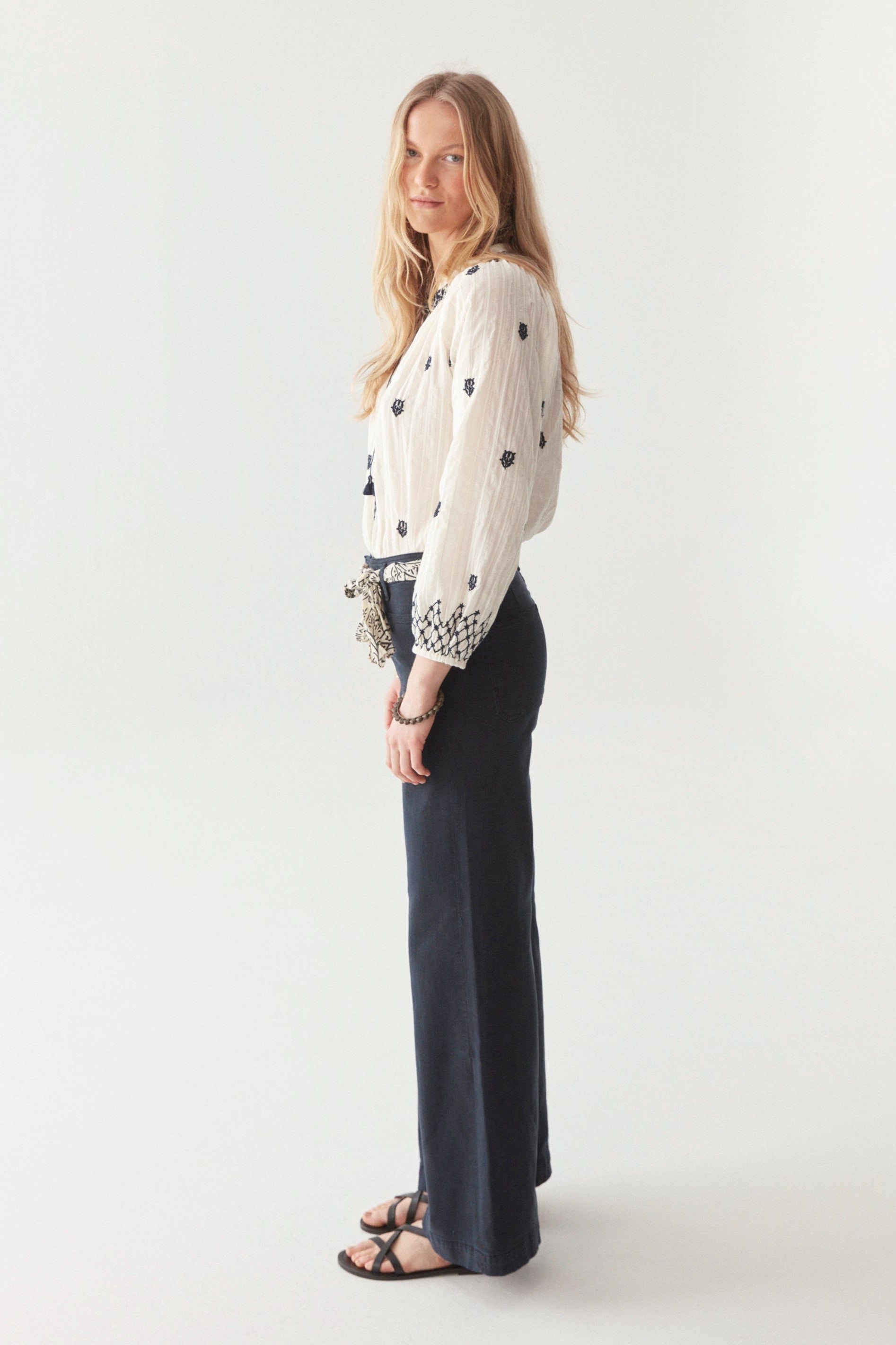 White cotton blouse with smocked neckline and navy embroidery all over with front tassels on model.  