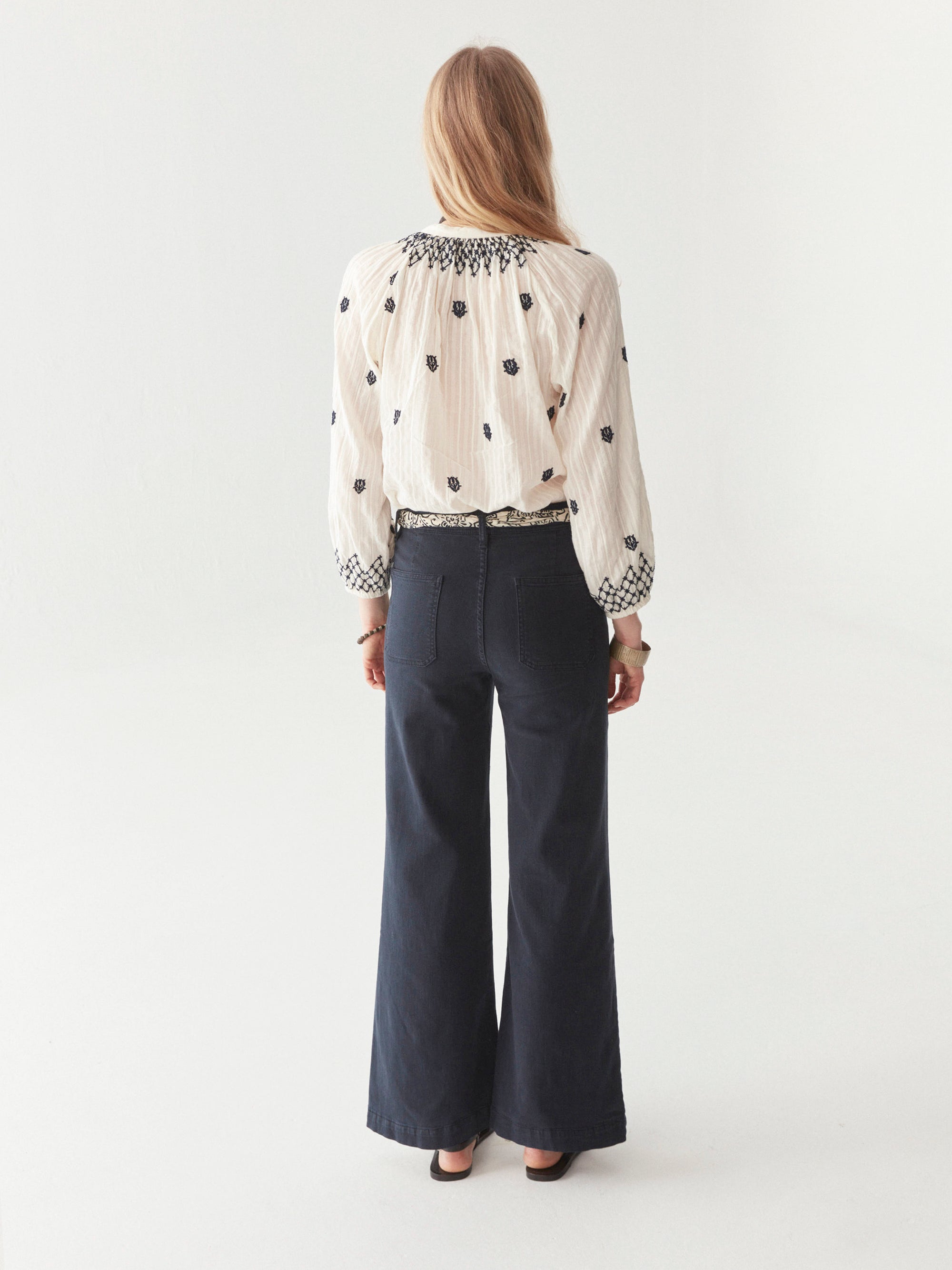White cotton blouse with smocked neckline and navy embroidery all over with front tassels on model.  