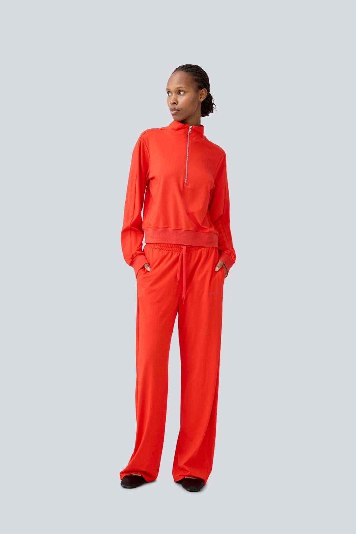 Model in wearing a bright red track suit pant and top set on a light gray background