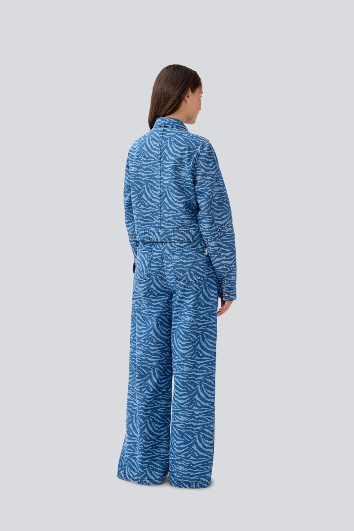 Model wearing a blue zebra print shirt and pant set to show back on a light gray background