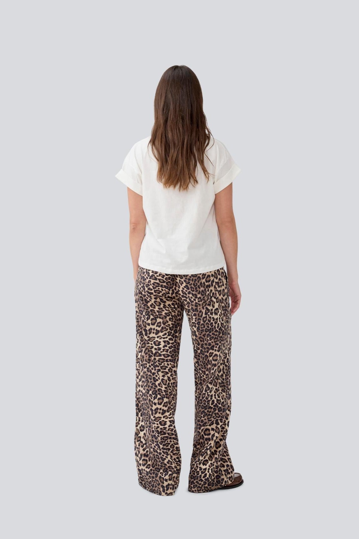 Person wearing a white t-shirt and leopard print pants on a light gray background