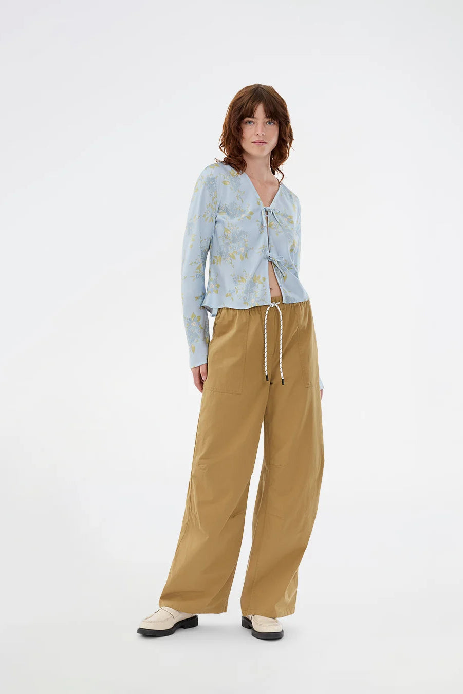Woman wearing a light blue floral shirt and tan pants on a white background