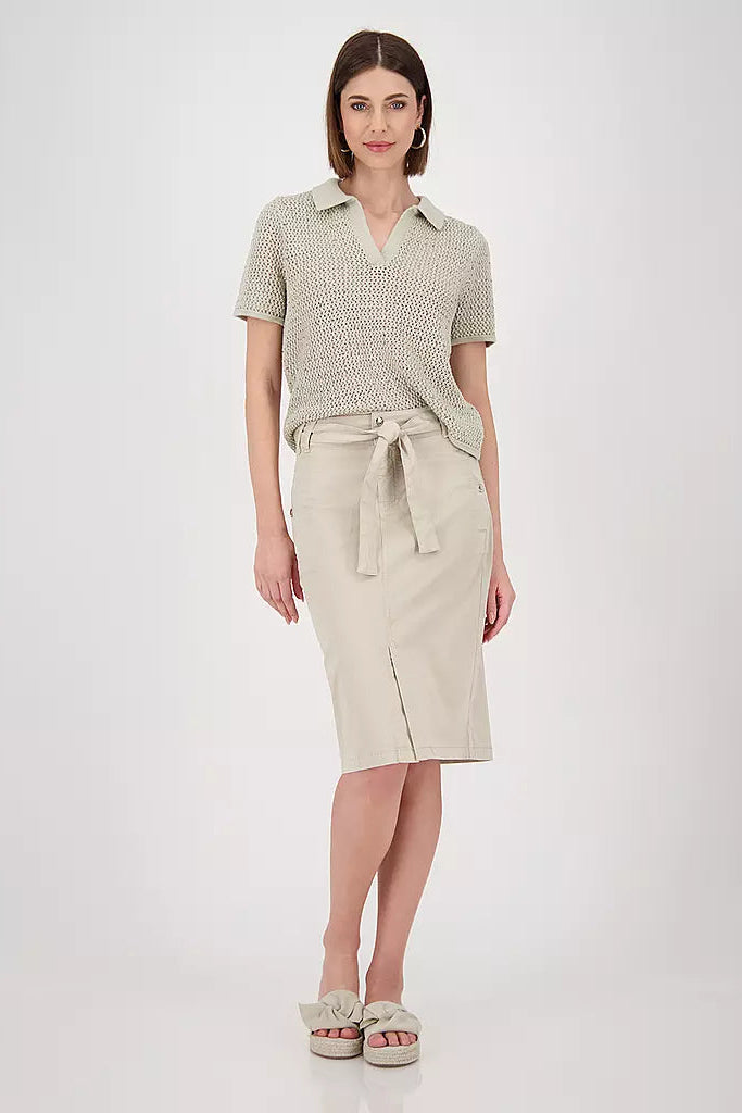 Woman wearing a patterned beige knit polo shirt and beige skirt on a white background