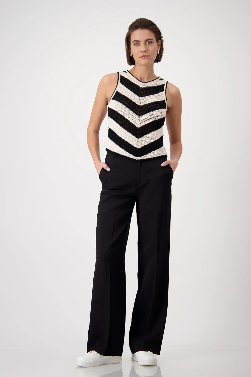 Woman wearing a black and white striped sleeveless top and black pants on a white background