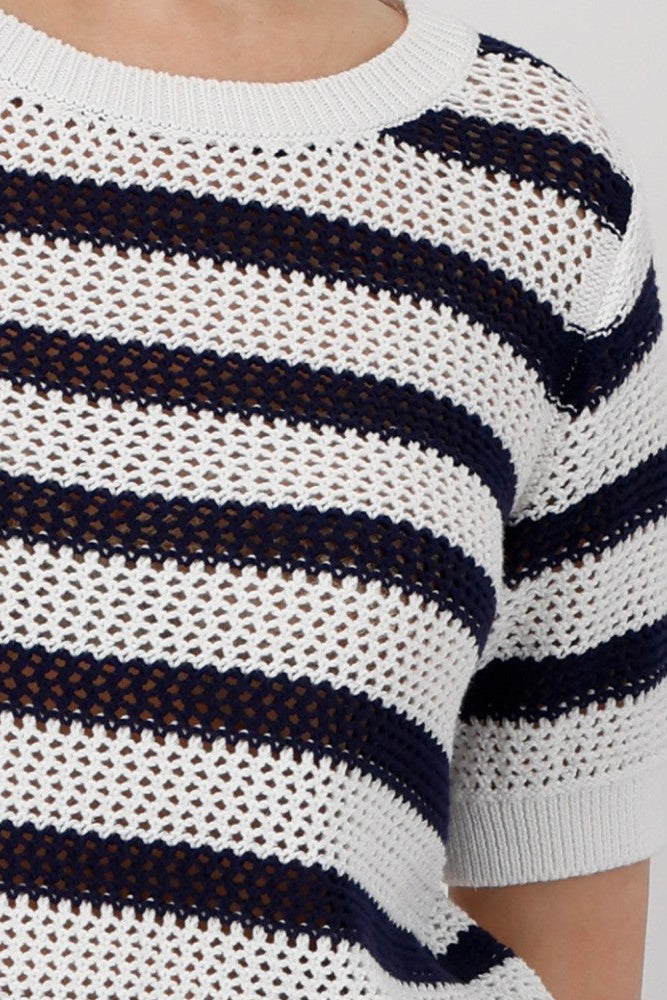 Woman wearing a navy and white striped short sleeve knit top with navy pants on a plain background