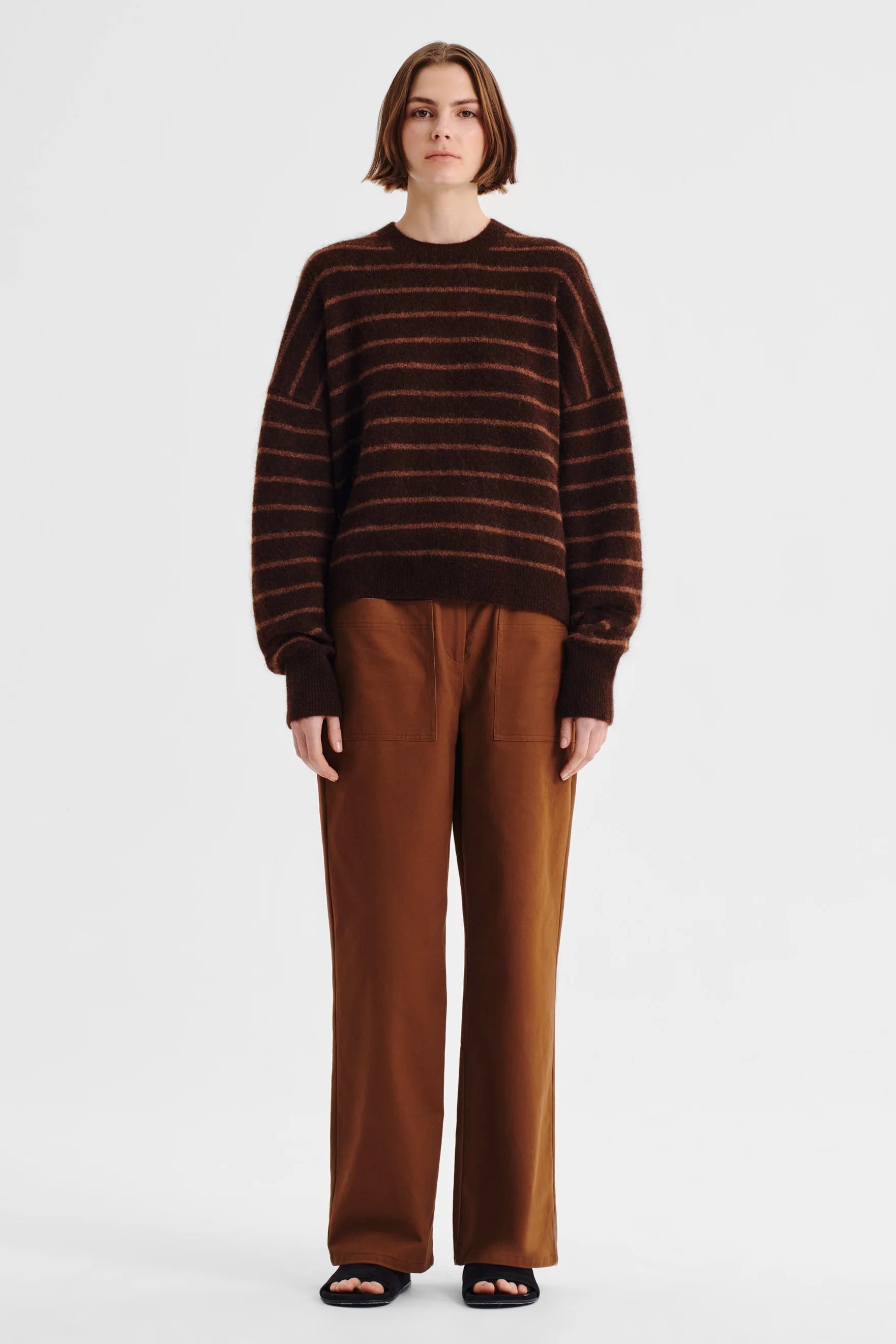 Women wearing brown knit with pink stripe and tan pants on a white background. 