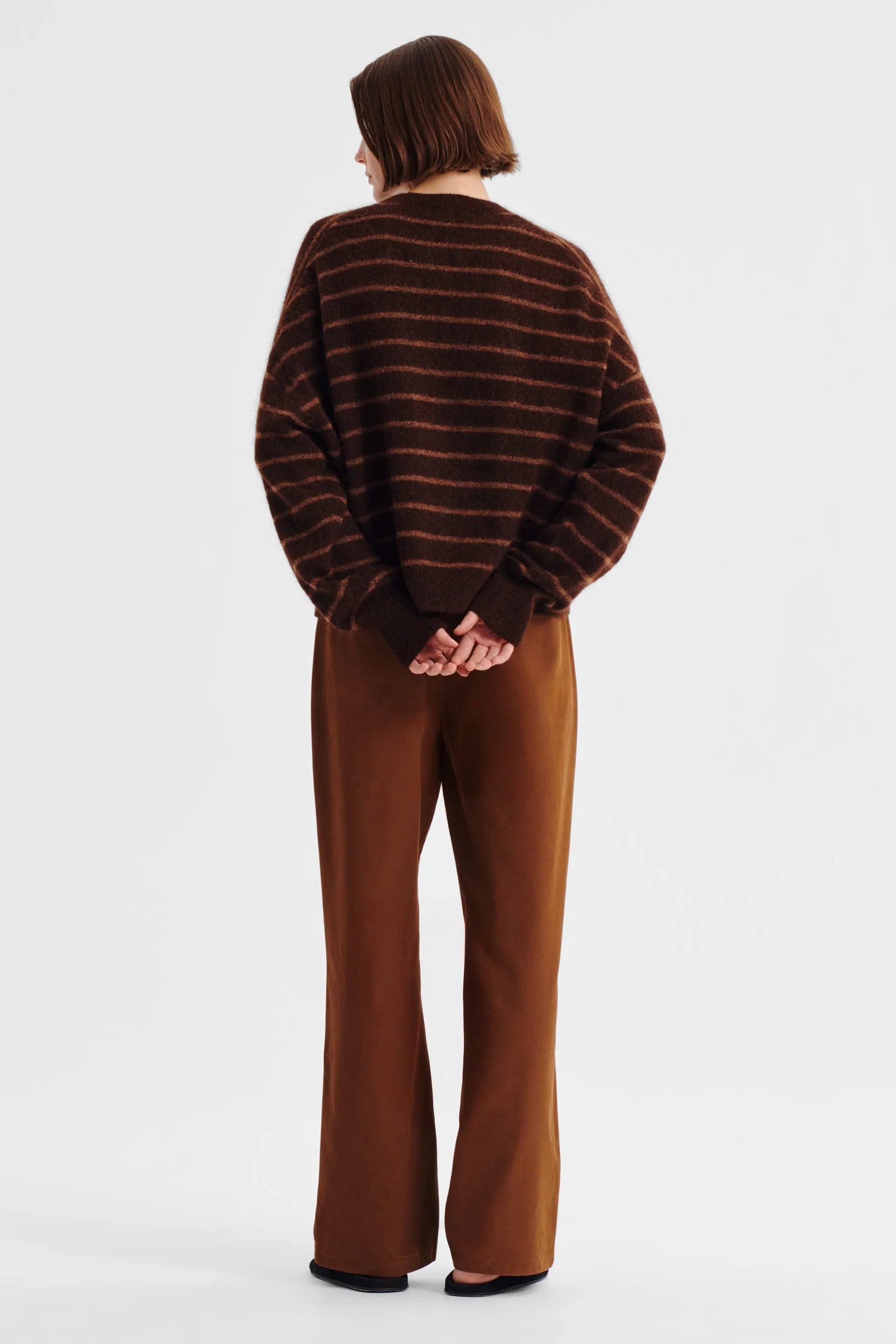 Women wearing brown knit with pink stripe and tan pants on a white background. 