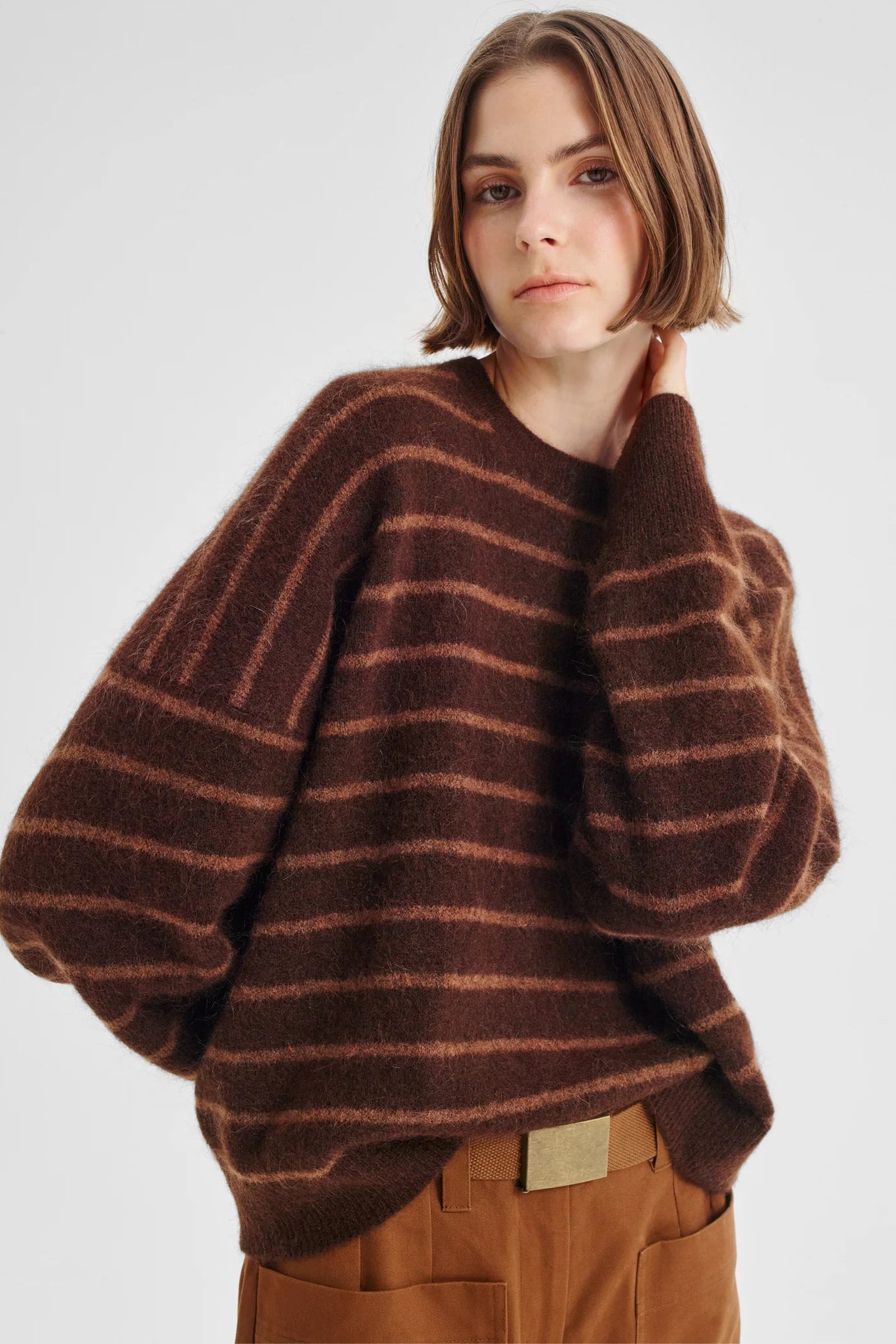 Women wearing brown knit with pink stripe and tan pants on a white background. 