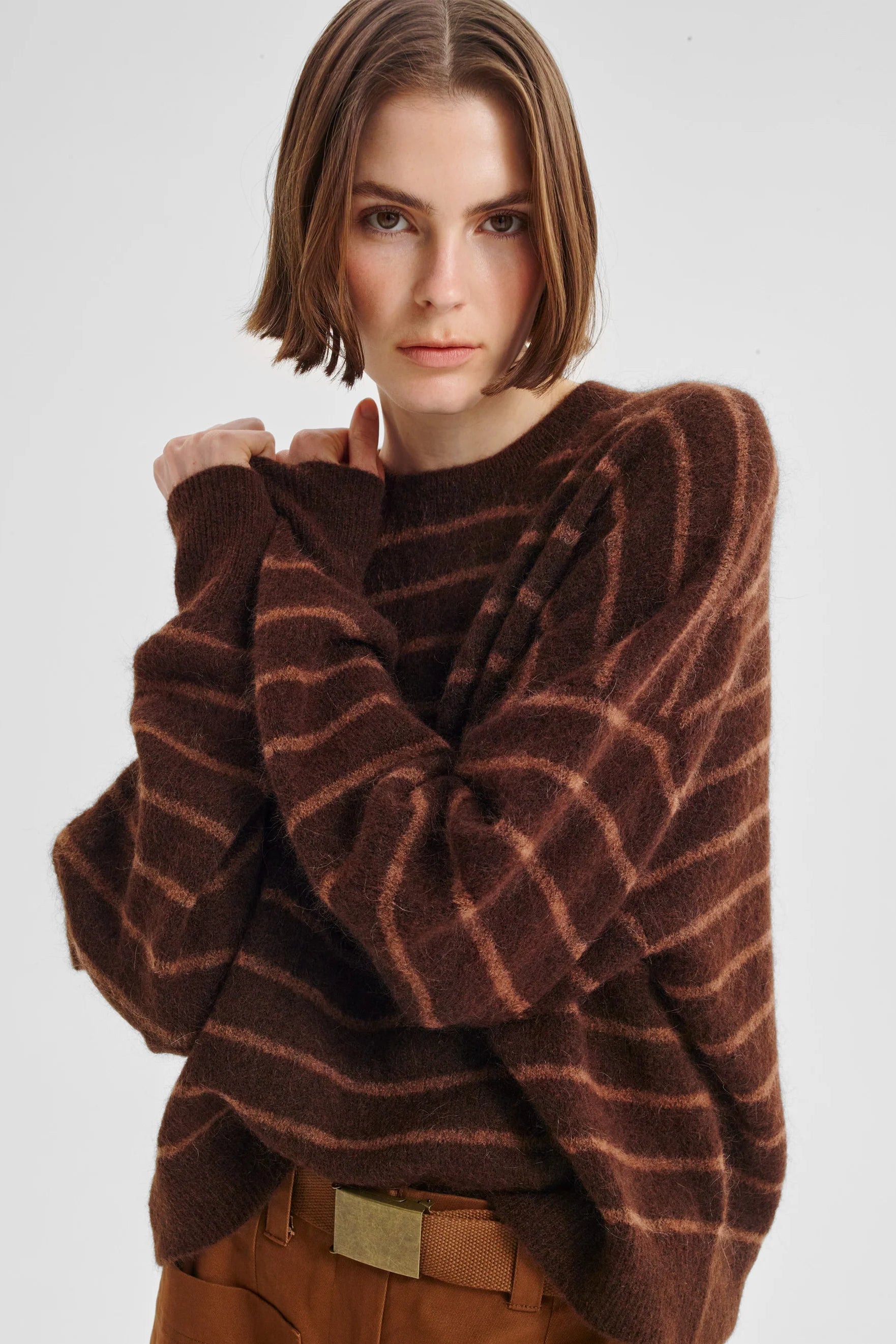 Women wearing brown knit with pink stripe and tan pants on a white background. 
