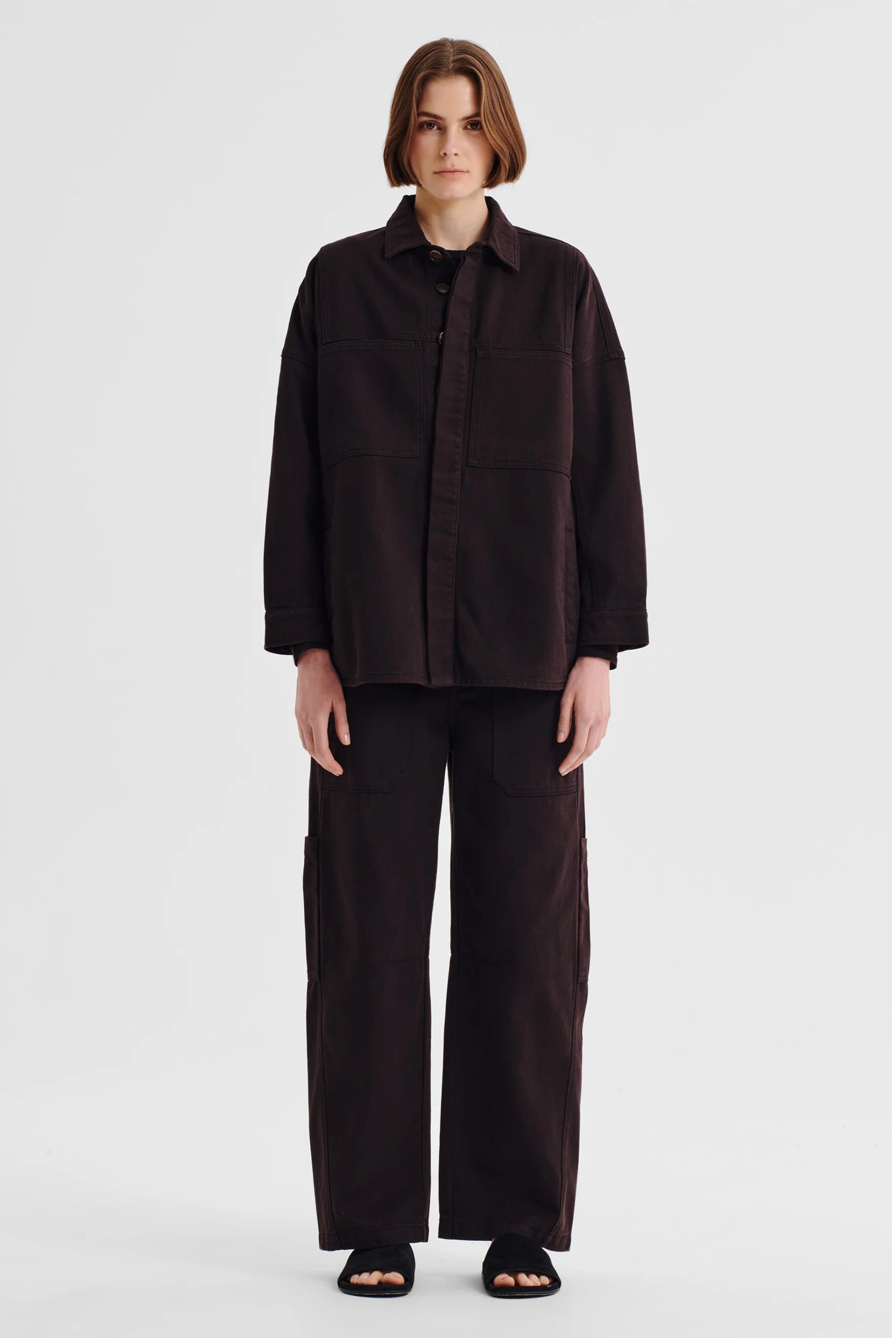Women wearing dark brown denim shirt jacket and matching denim pant on a white background. 